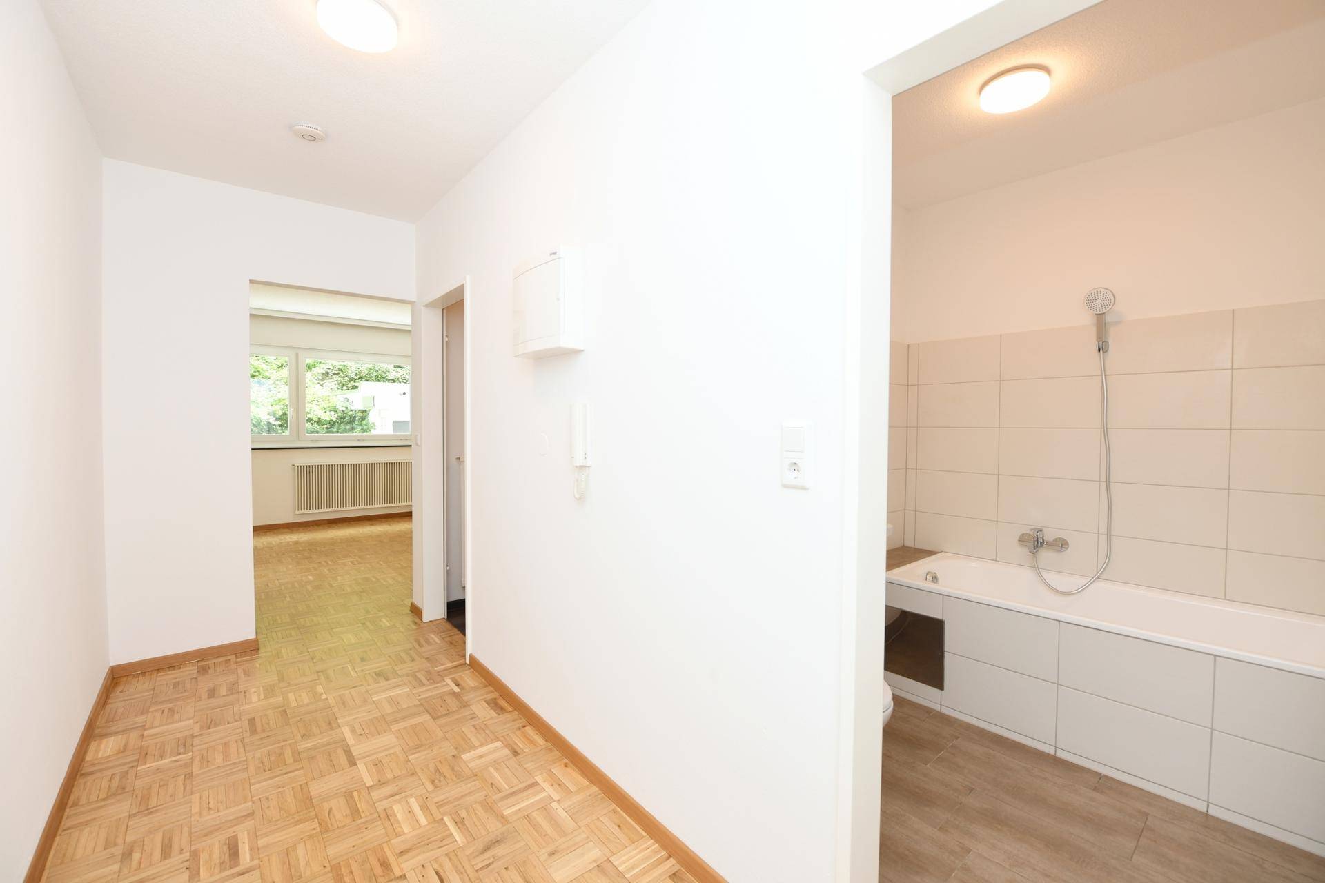 Heller Flur mit Parkettboden und offenem Blick in das Badezimmer und einen weiteren Raum.