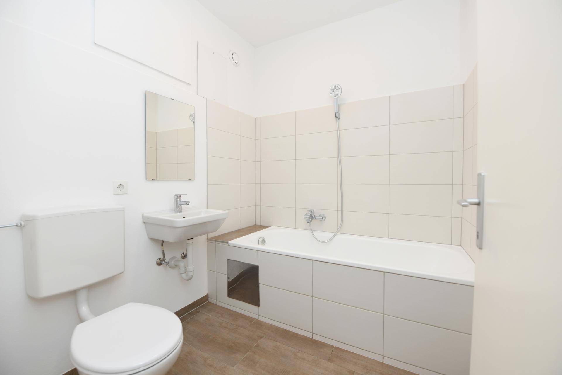 Helles Badezimmer mit Badewanne, WC, Waschbecken und weißen Wandfliesen.