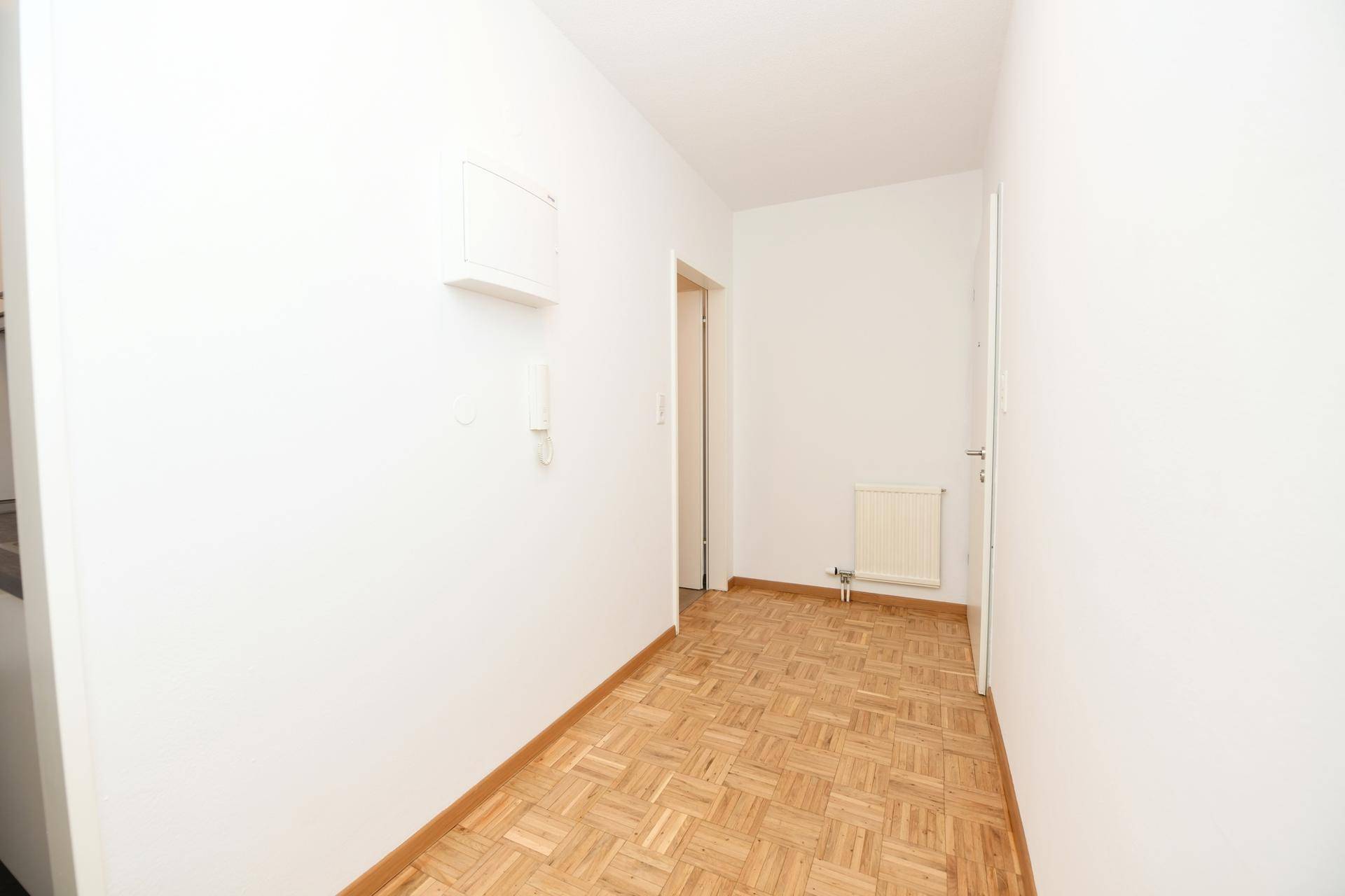 Schlichter Flur mit hellem Parkettboden und weißen Wänden.