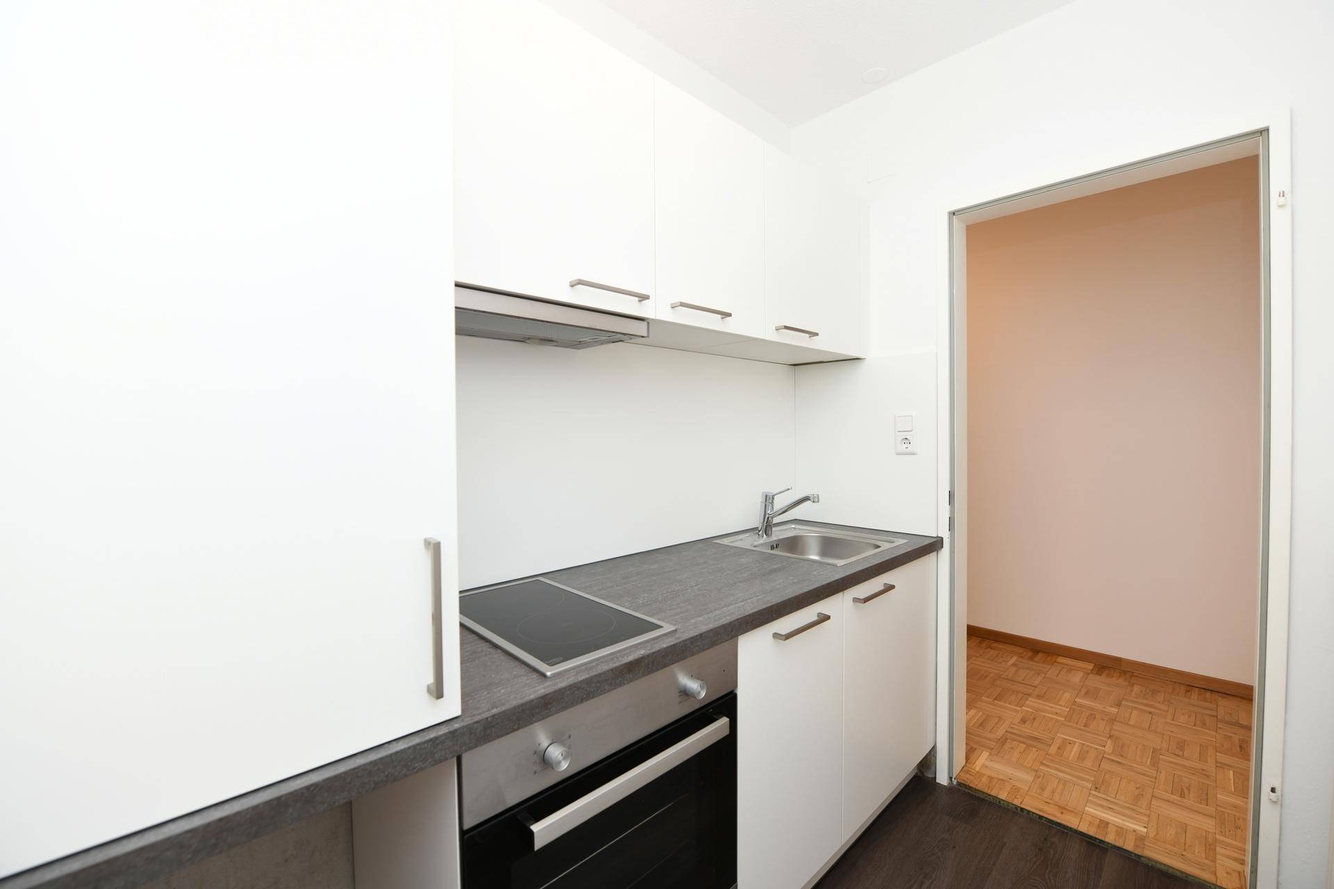Funktionale Küchenzeile mit weißen Fronten und Blick in den angrenzenden Wohnbereich.