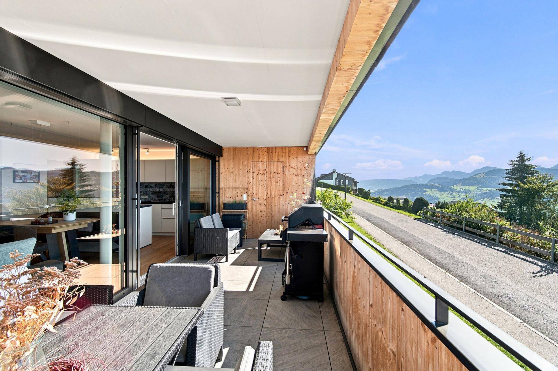 Moderne Balkonterrasse mit Holzwänden, Essbereich und Grill, bietet einen weiten Blick auf die Berge.