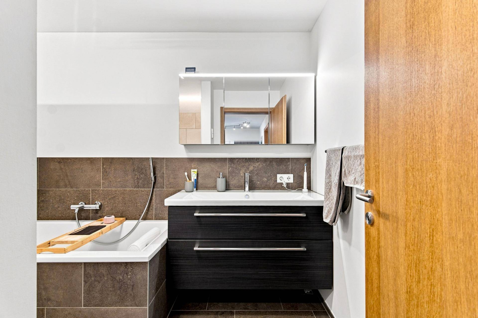 Modernes Badezimmer mit Badewanne, Waschtischunterschrank und beleuchtetem Spiegelschrank.