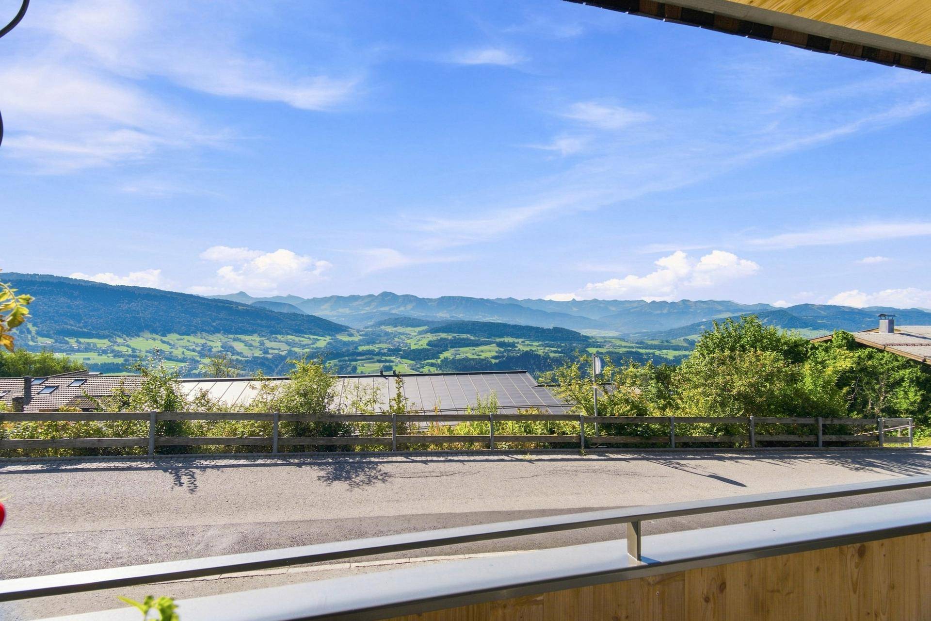 Panoramablick von einem Balkon auf die weite grüne Hügellandschaft und ferne Berge unter blauem Himmel.