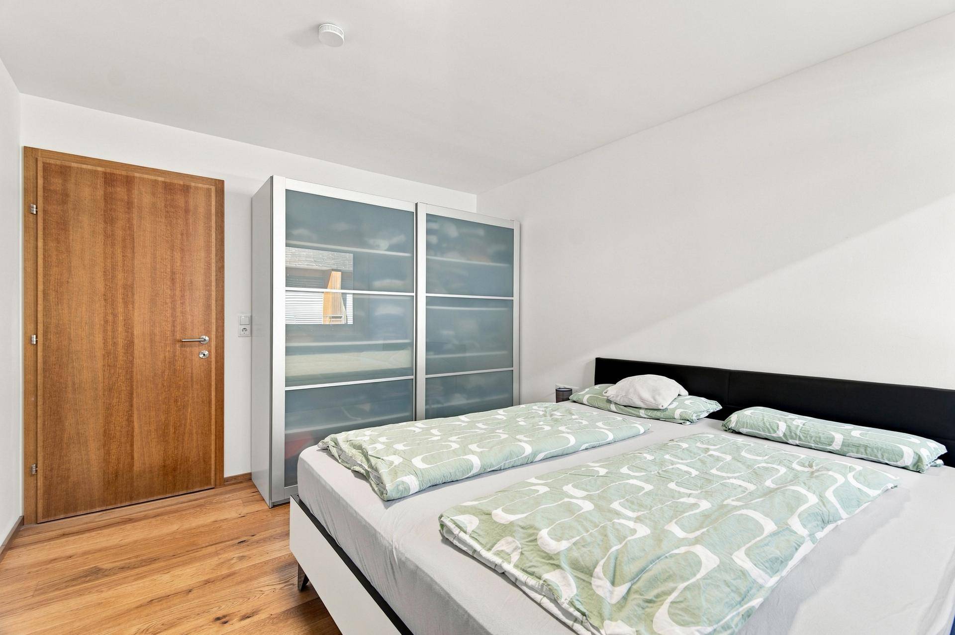 Schlafzimmer mit Holzboden, Doppelbett und einem modernen Kleiderschrank mit Schiebetüren.