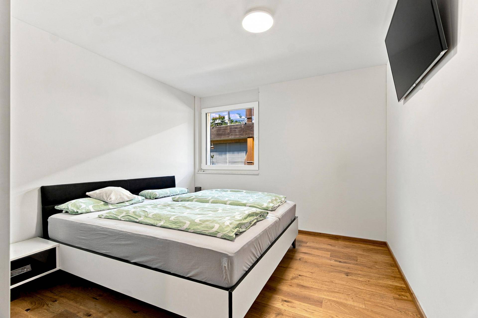 Gemütliches Schlafzimmer mit Doppelbett, Holzboden und einem Fenster, das Tageslicht hereinlässt.