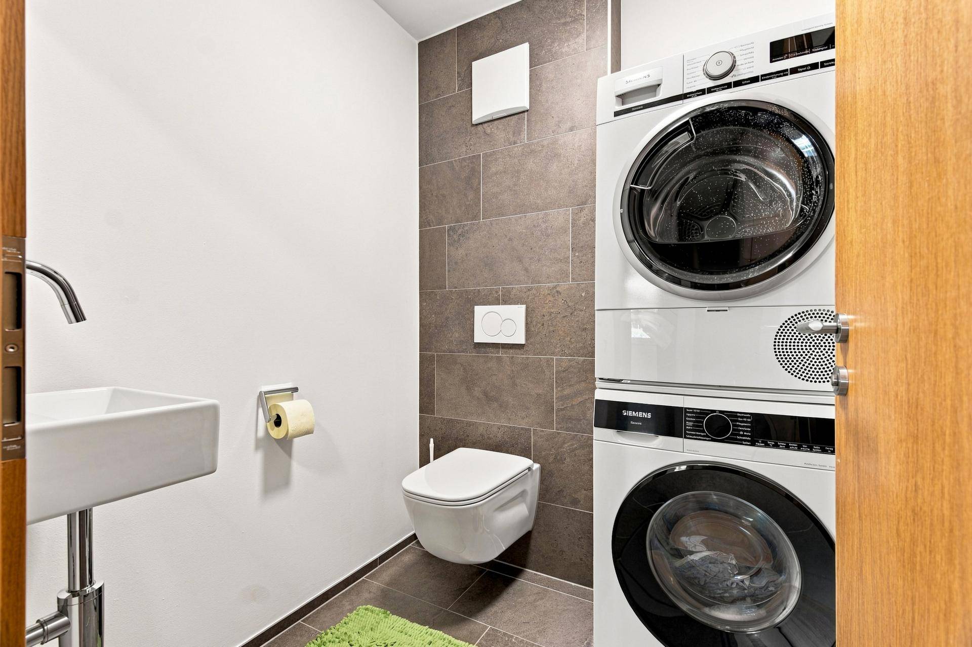 Modernes Gäste-WC mit Wand-WC, Waschbecken und integrierter Waschmaschine und Trockner.