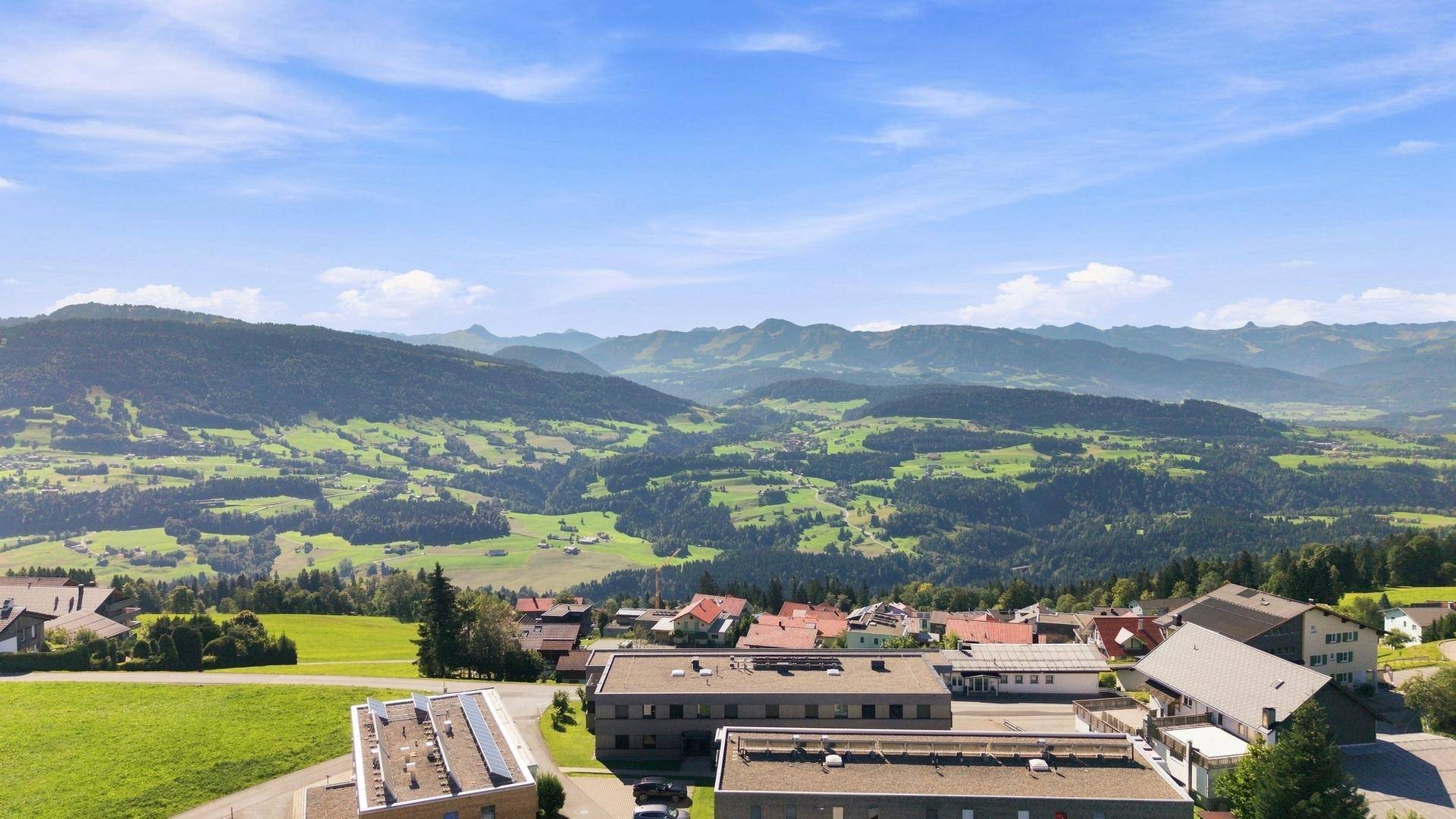 Panoramische Luftaufnahme einer ländlichen Gegend mit verstreuten Häusern und weiten grünen Tälern.