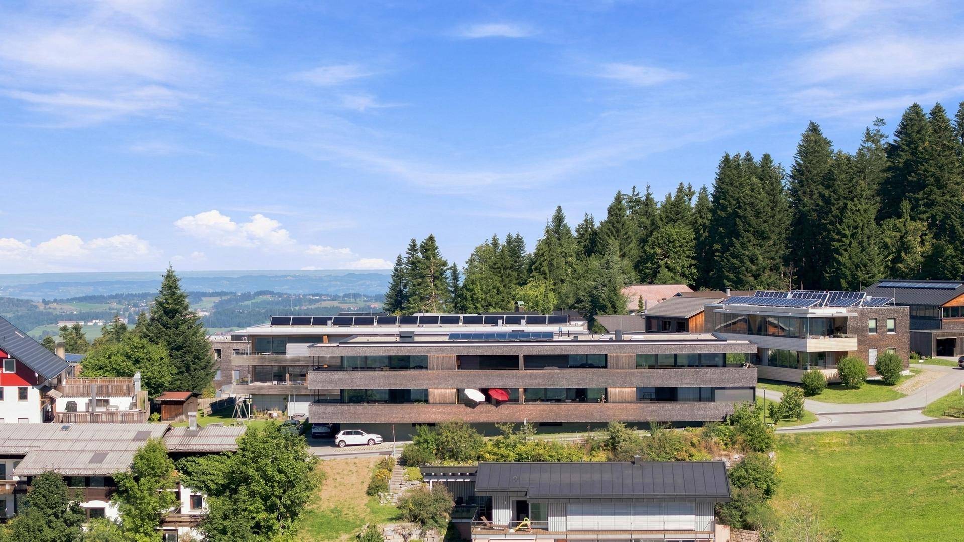 Modernes Apartmentgebäude mit Holzfassade und Balkonen, eingebettet in eine grüne Hügellandschaft.