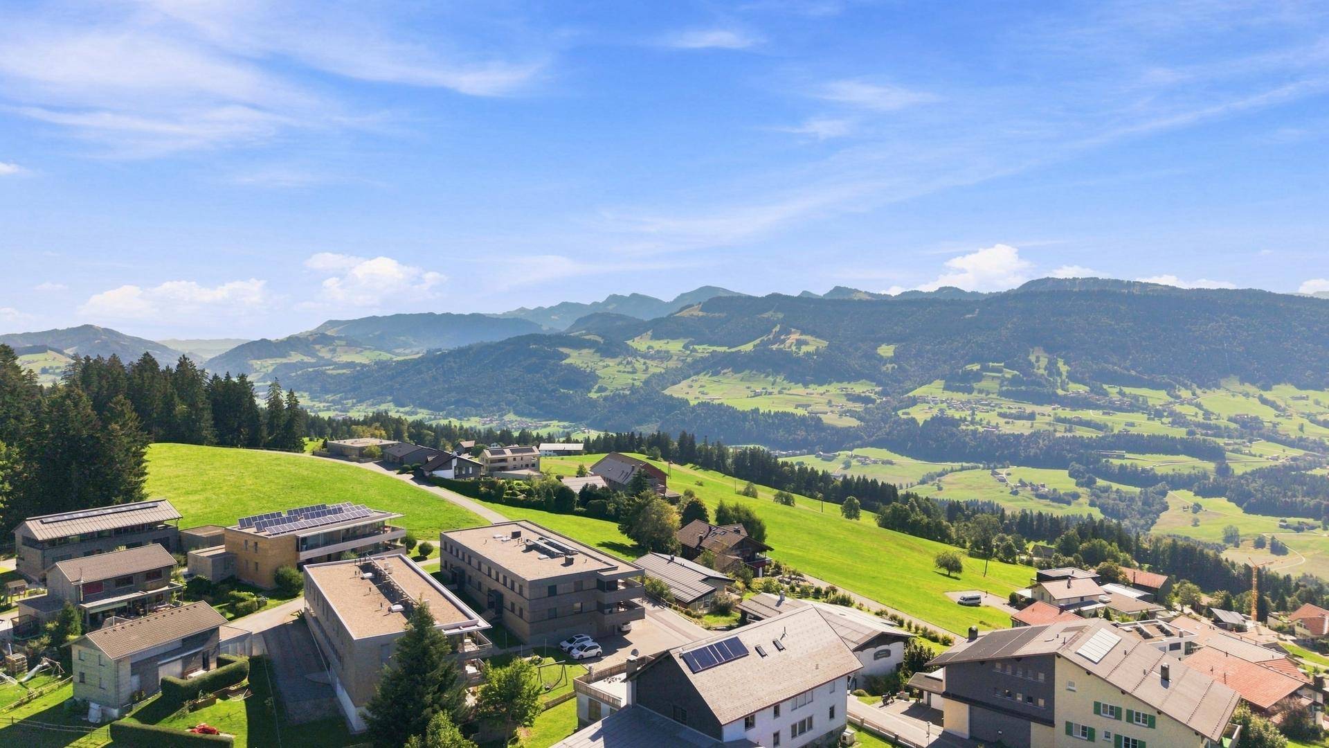 Luftaufnahme einer ländlichen Siedlung mit verschiedenen Gebäuden und weiten grünen Feldern im Vordergrund.