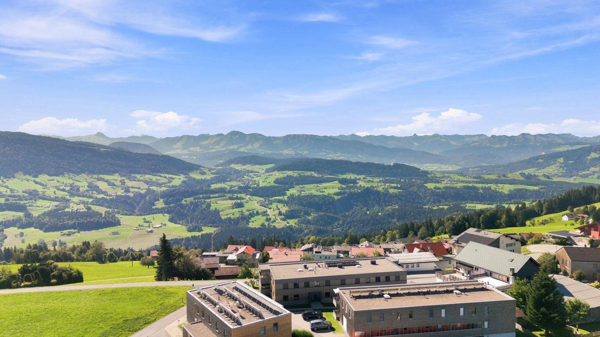 Panoramablick aus der Vogelperspektive auf eine malerische grüne Hügellandschaft mit verstreuten Häusern.
