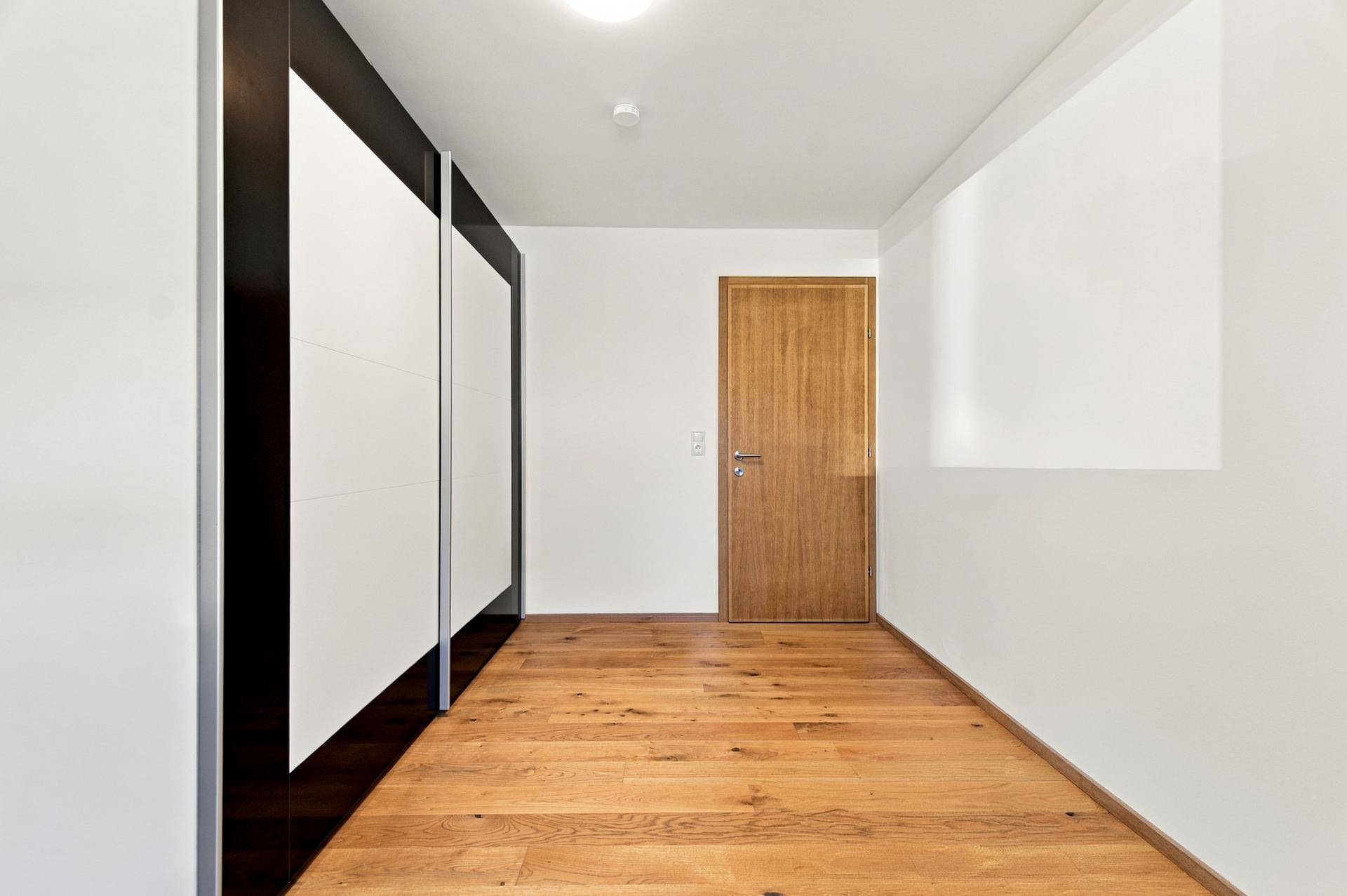 Heller Flur mit Holzboden und einem großen Schiebetürenschrank, der viel Stauraum bietet.