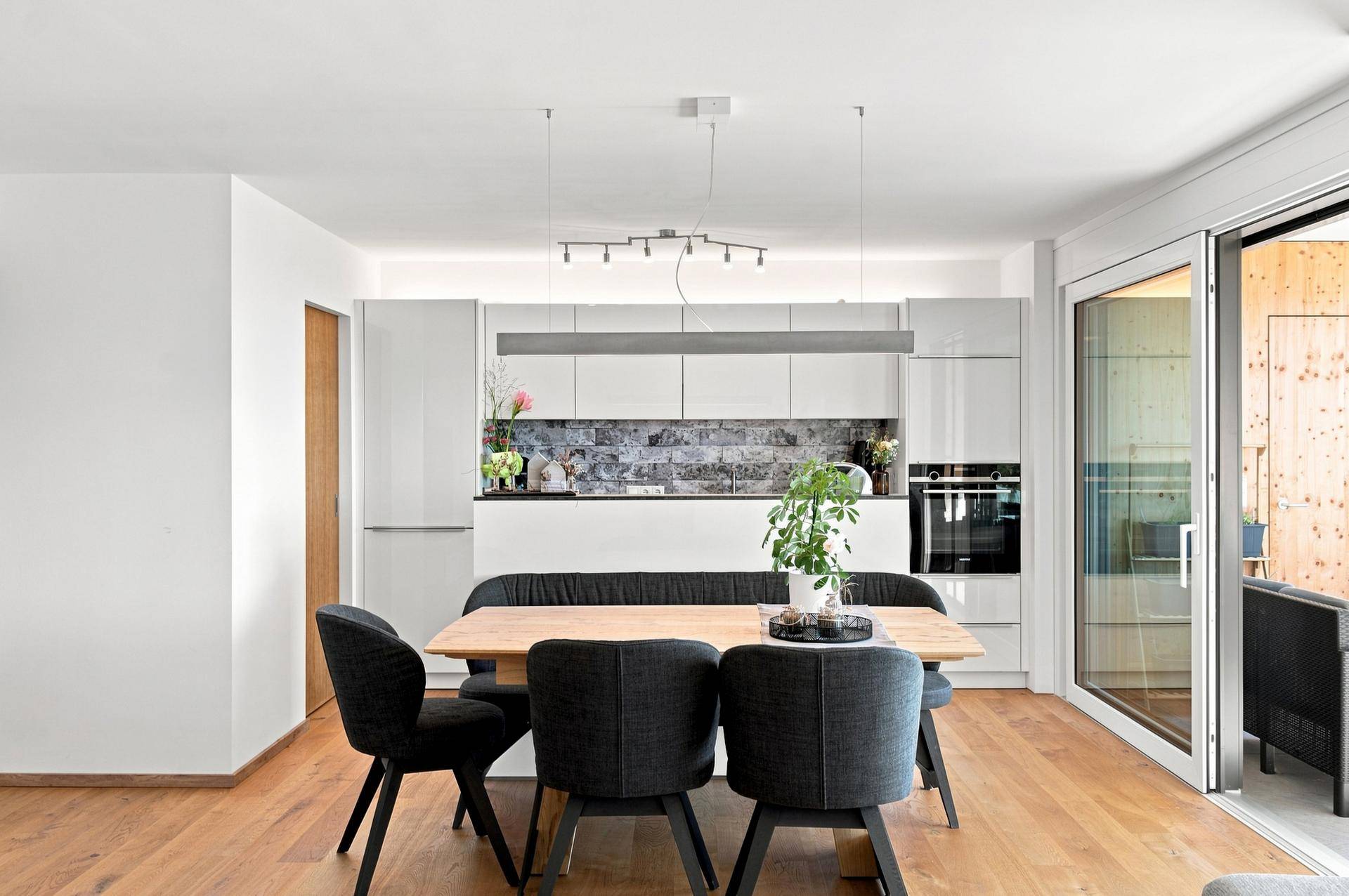 Moderne Einbauküche mit weißen Fronten, dunkler Arbeitsplatte und Essbereich mit Holztisch.
