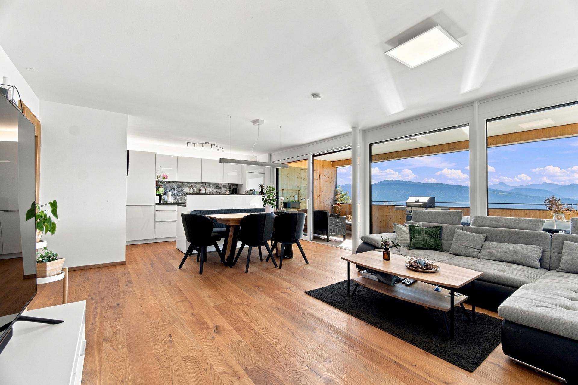 Moderner offener Wohnbereich mit integrierter Küche, Holzboden und Zugang zur Terrasse mit Bergblick.