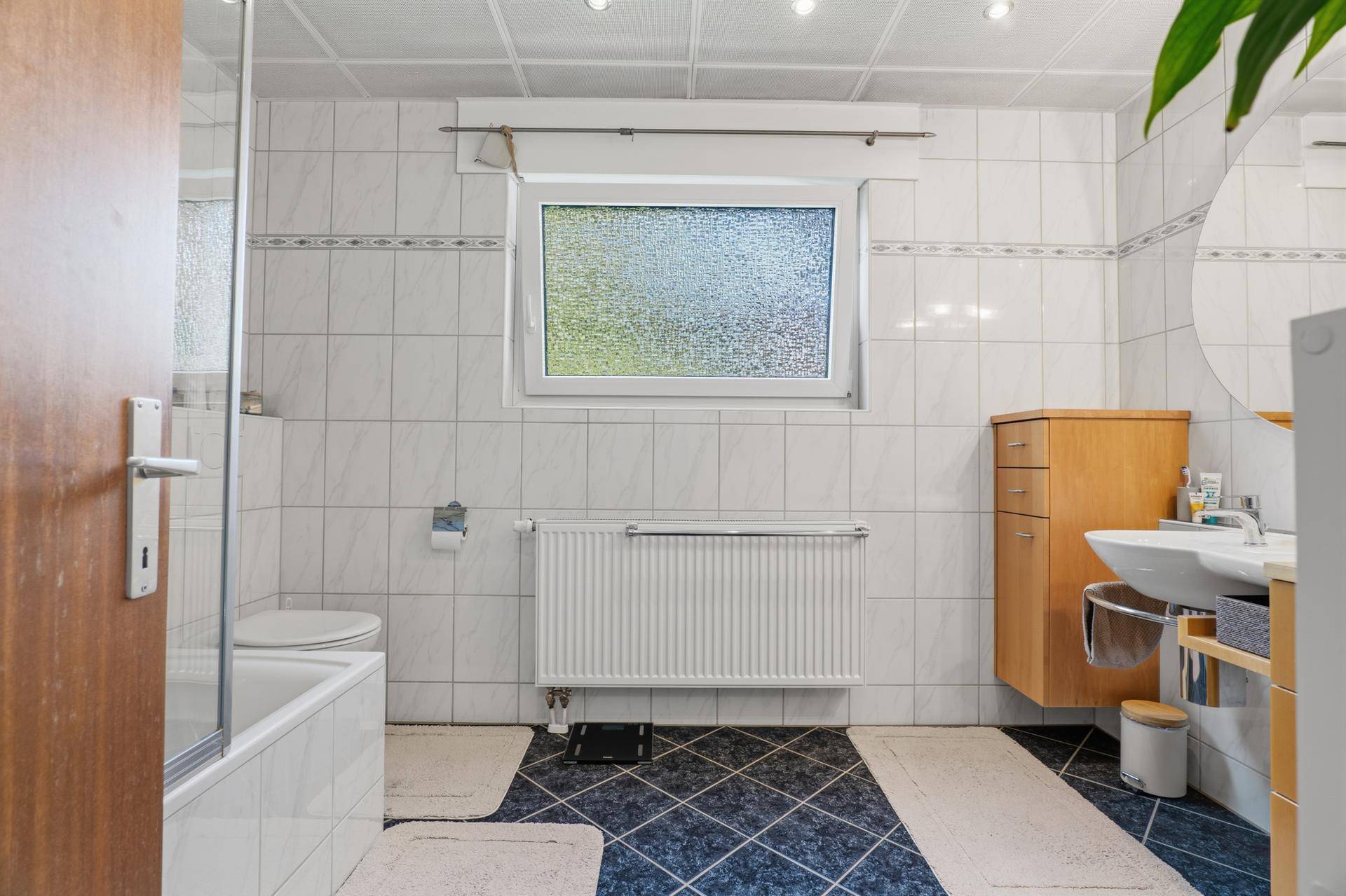 Gefliestes Badezimmer mit Badewanne, Duschabtrennung und Fenster.