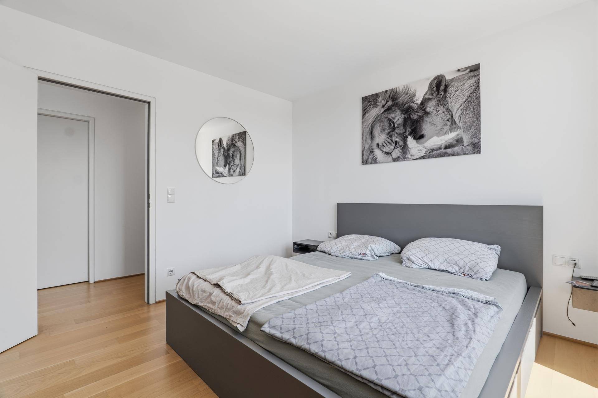 Helles Schlafzimmer mit schlichtem Design, Holzboden und Zugang zum Flur.