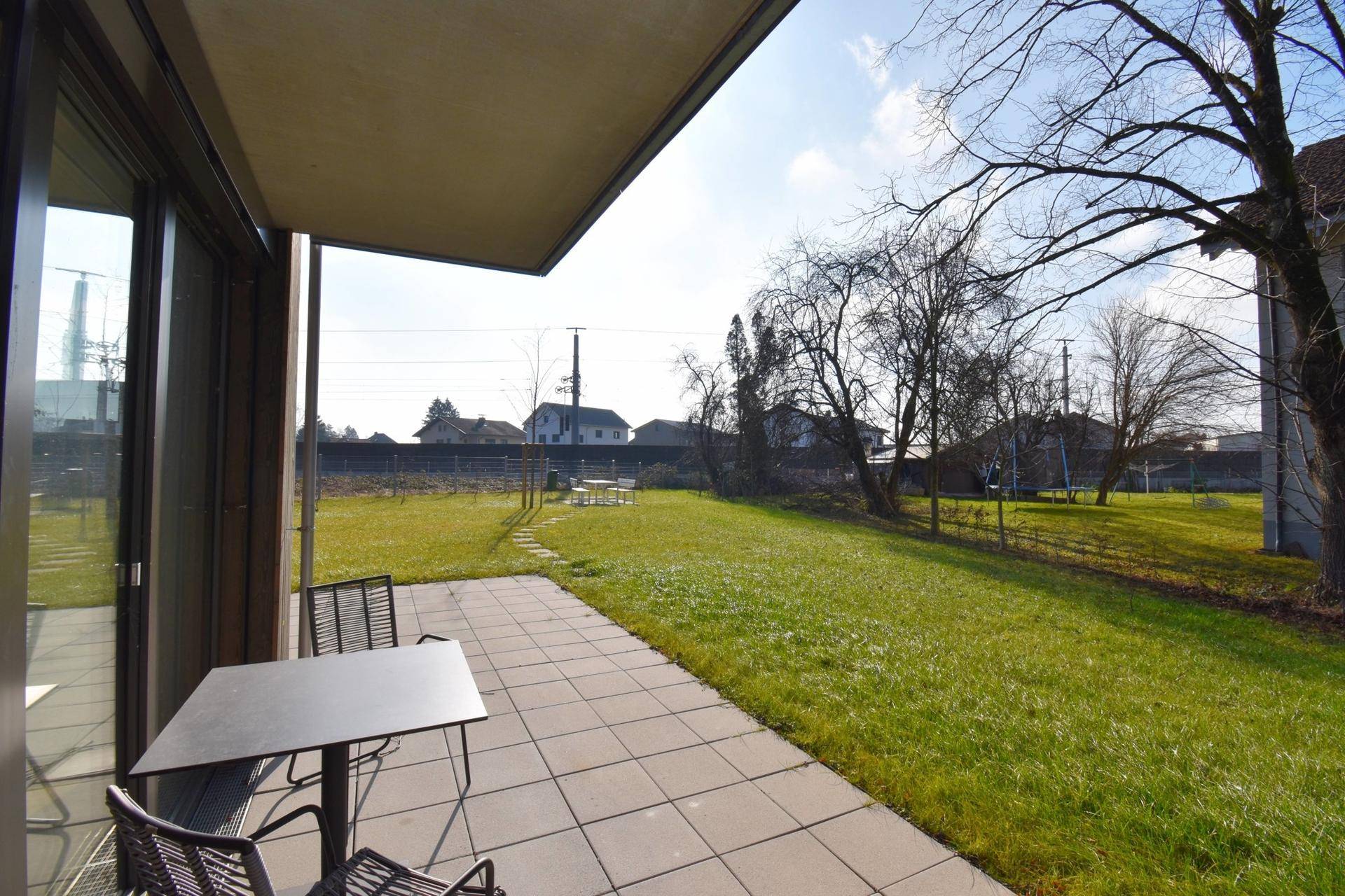 Sonniger Außenbereich mit Terrasse, Rasen und Bäumen, ideal zum Entspannen und Verweilen.