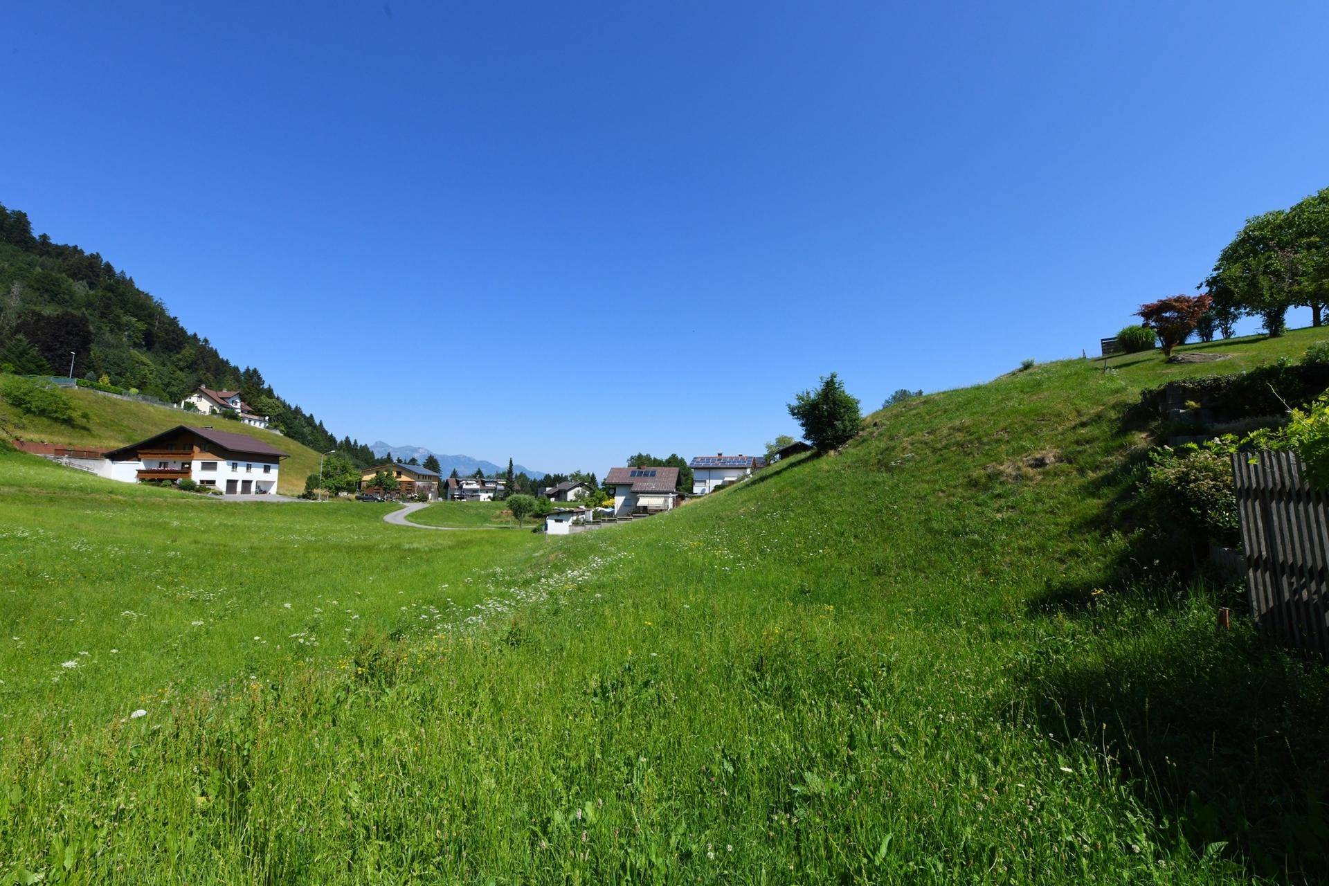 Weitläufiger Blick über ein grünes Tal mit verstreuten Häusern und klarem blauen Himmel.