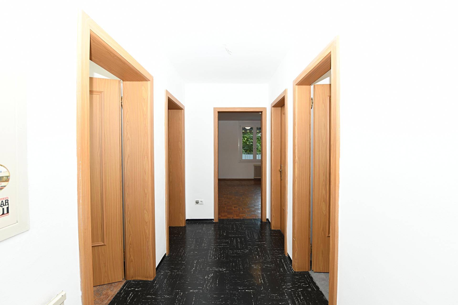 Langer, heller Flur mit dunklem Fliesenboden und mehreren Holztüren zu den Zimmern.