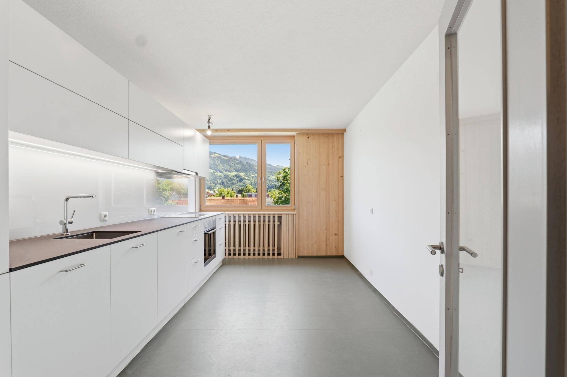 Moderne Einbauküche mit weißen Schränken, dunkler Arbeitsplatte und Bergblick.