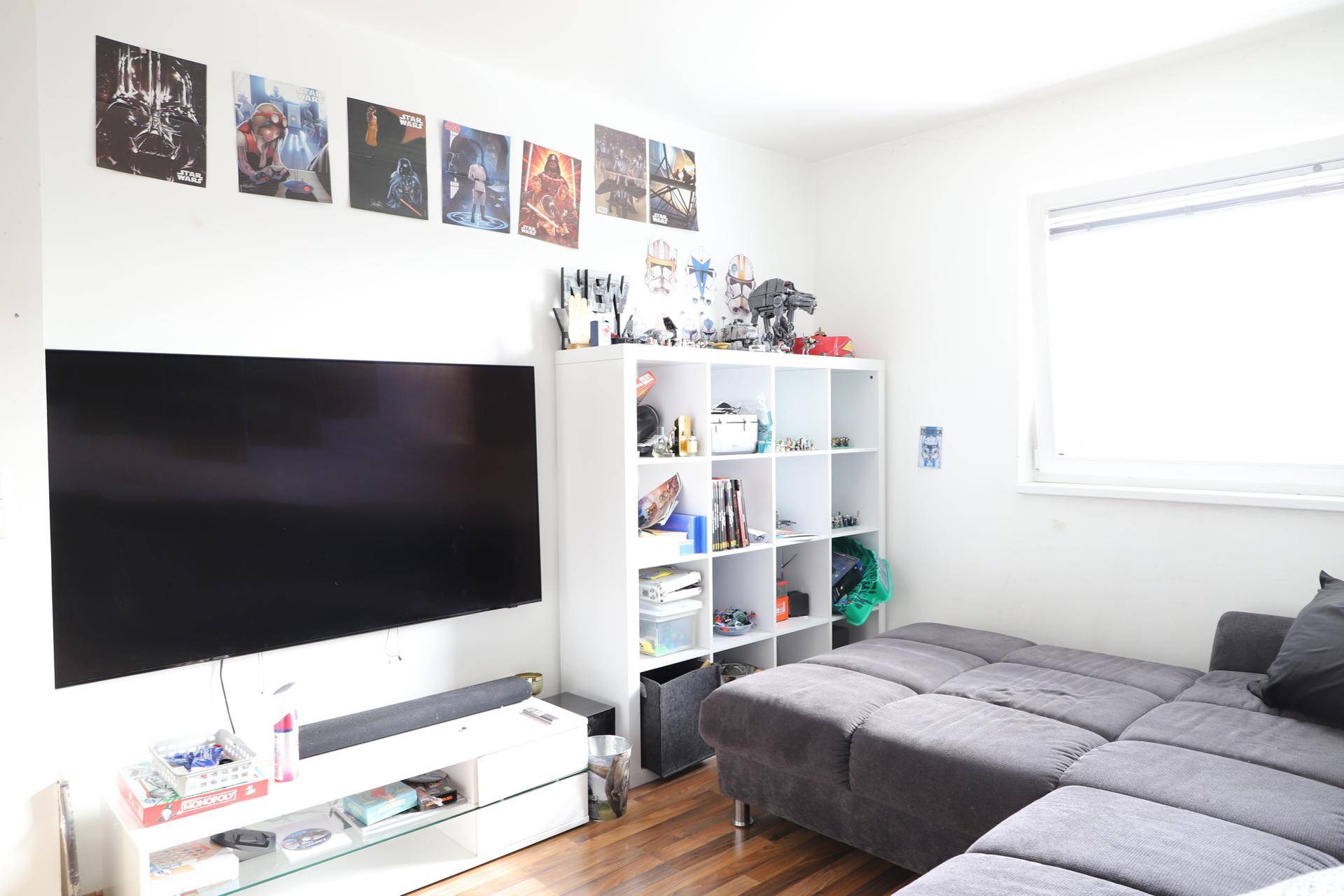 Kinder- oder Gästezimmer mit großem Fernseher, Regalsystem und gemütlichem Sofa.