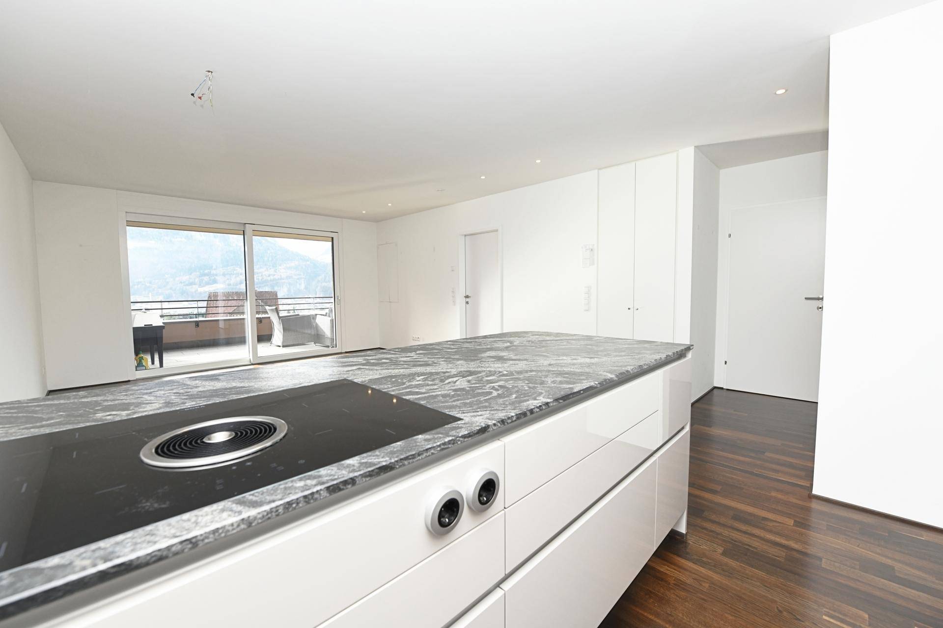 Moderne Küche mit Kücheninsel und Blick auf den Wohnbereich und den Balkon.