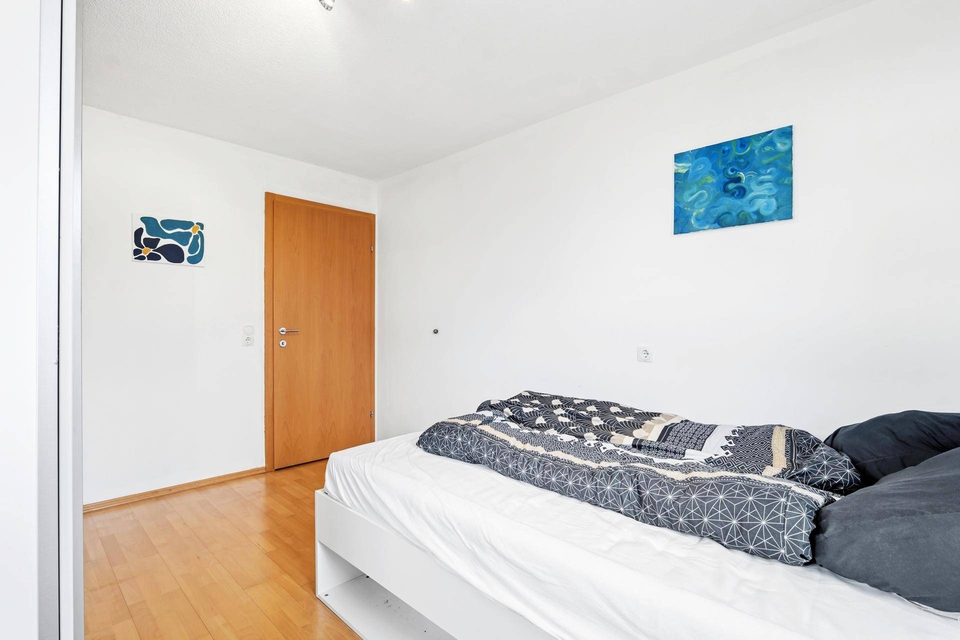 Schlafzimmer mit Holzboden, weißem Bett und minimalistischer Dekoration.