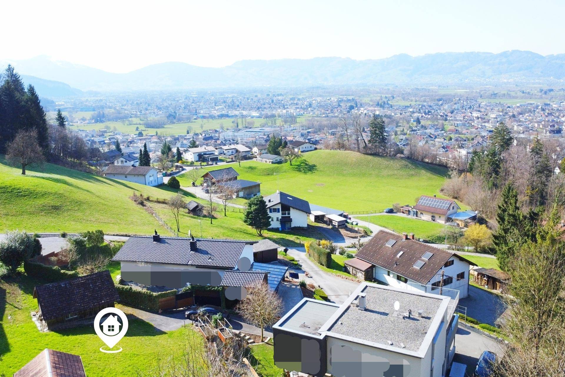 Weitläufiger Blick über eine ländliche Siedlung mit grünen Wiesen und einer Stadt am Horizont.