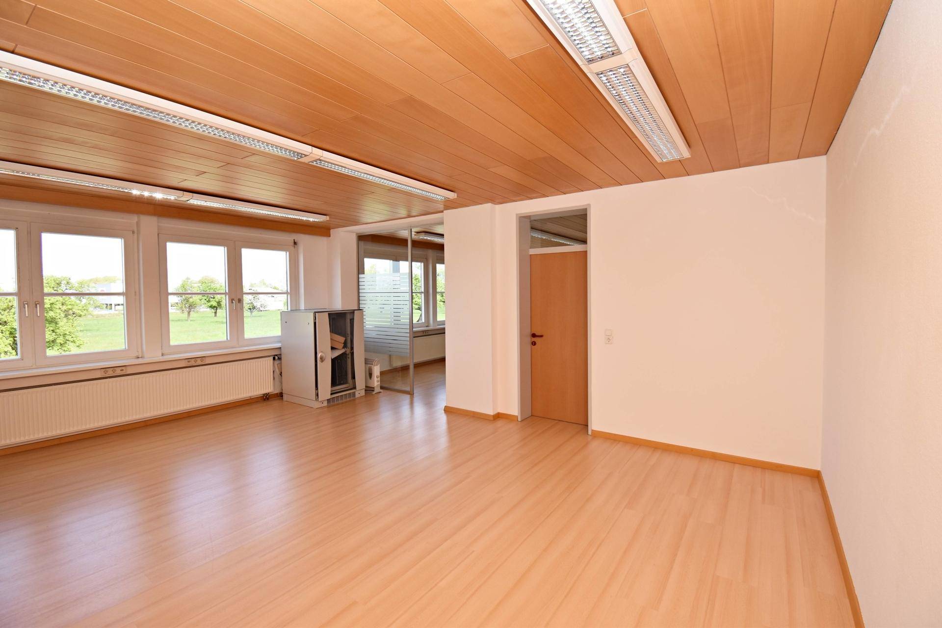 Heller Büroraum mit Laminatboden, Holzdecke und Blick auf die Umgebung, mit Schrank.