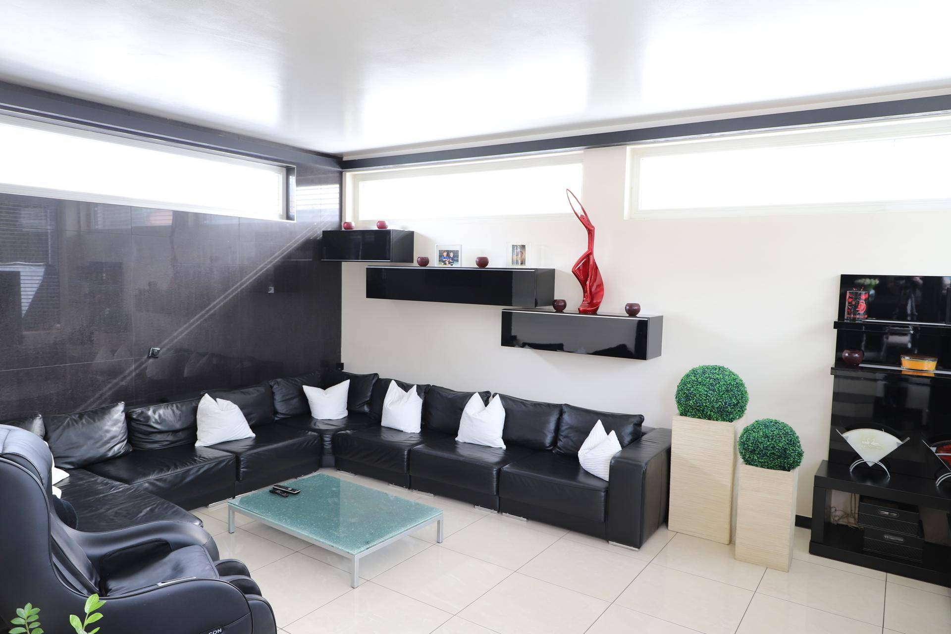 Geräumiges Wohnzimmer mit großer schwarzer Ledercouch, modernen Regalen und heller Atmosphäre.
