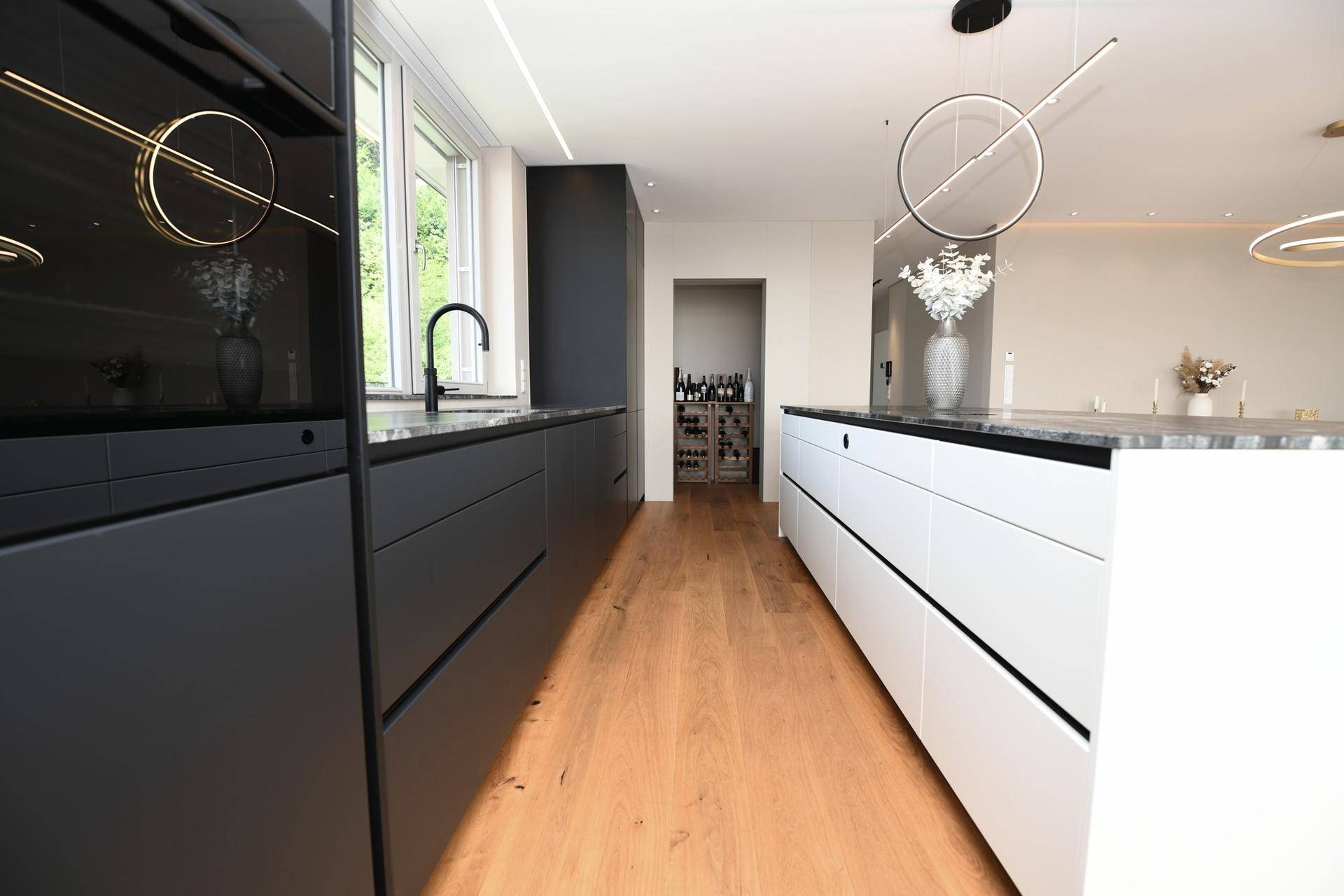 Elegante Küche mit schwarzer Schrankfront, weißer Kücheninsel und Holzboden.