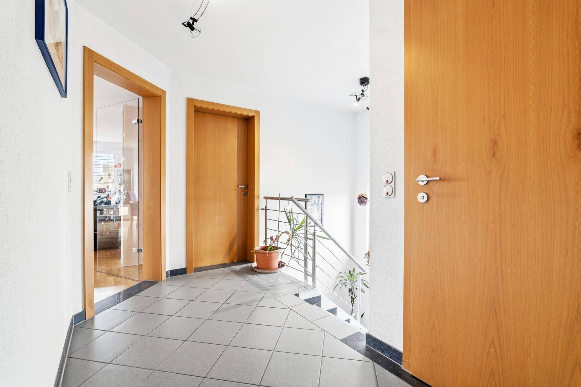 Heller Flur mit Fliesenboden und Holztreppe, die in die obere Etage führt.