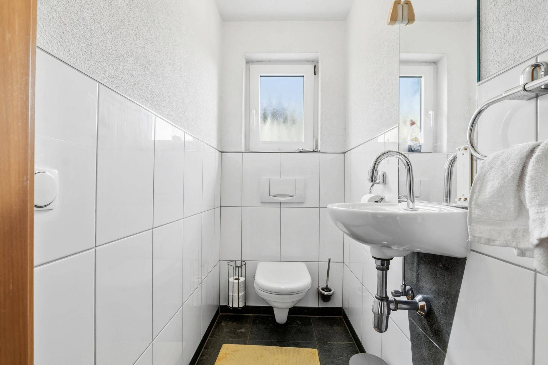Kleines Gäste-WC mit Fenster, Waschbecken und dunklem Fliesenboden.