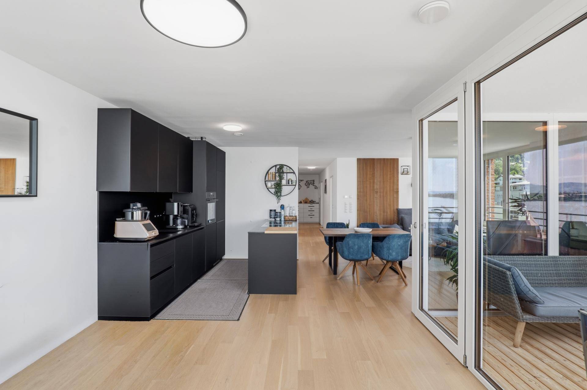 Heller Wohnbereich mit offener Küche und Zugang zu einem verglasten Balkon mit Seeblick.