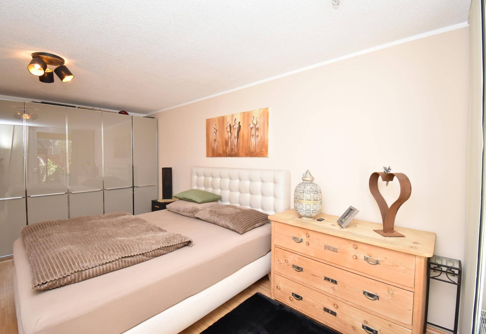 Gemütliches Schlafzimmer mit beigem Doppelbett, Holzkommode und großem Kleiderschrank.