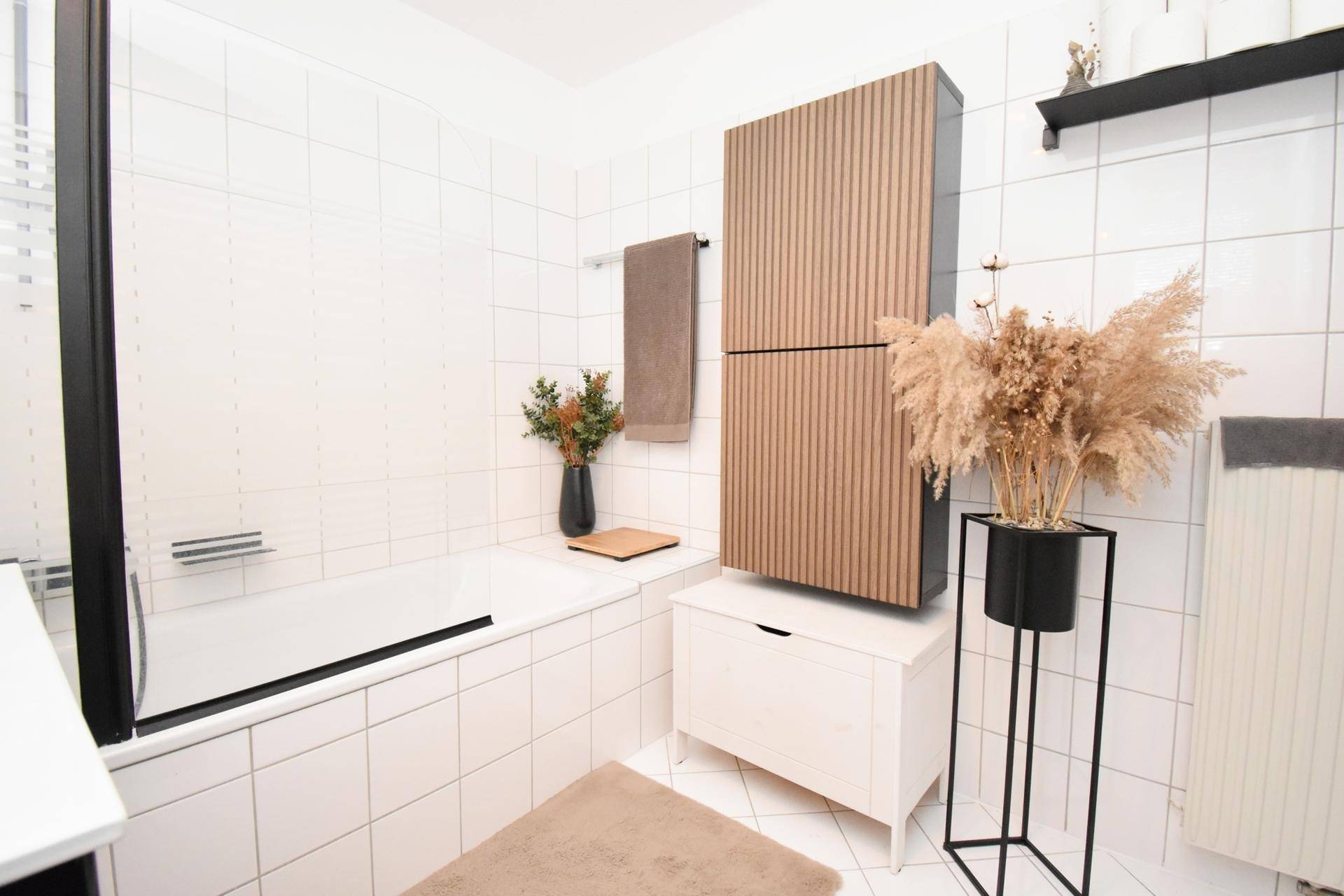 Helles Badezimmer mit Badewanne, weißen Wandfliesen und modernen Holzschränken für Stauraum.