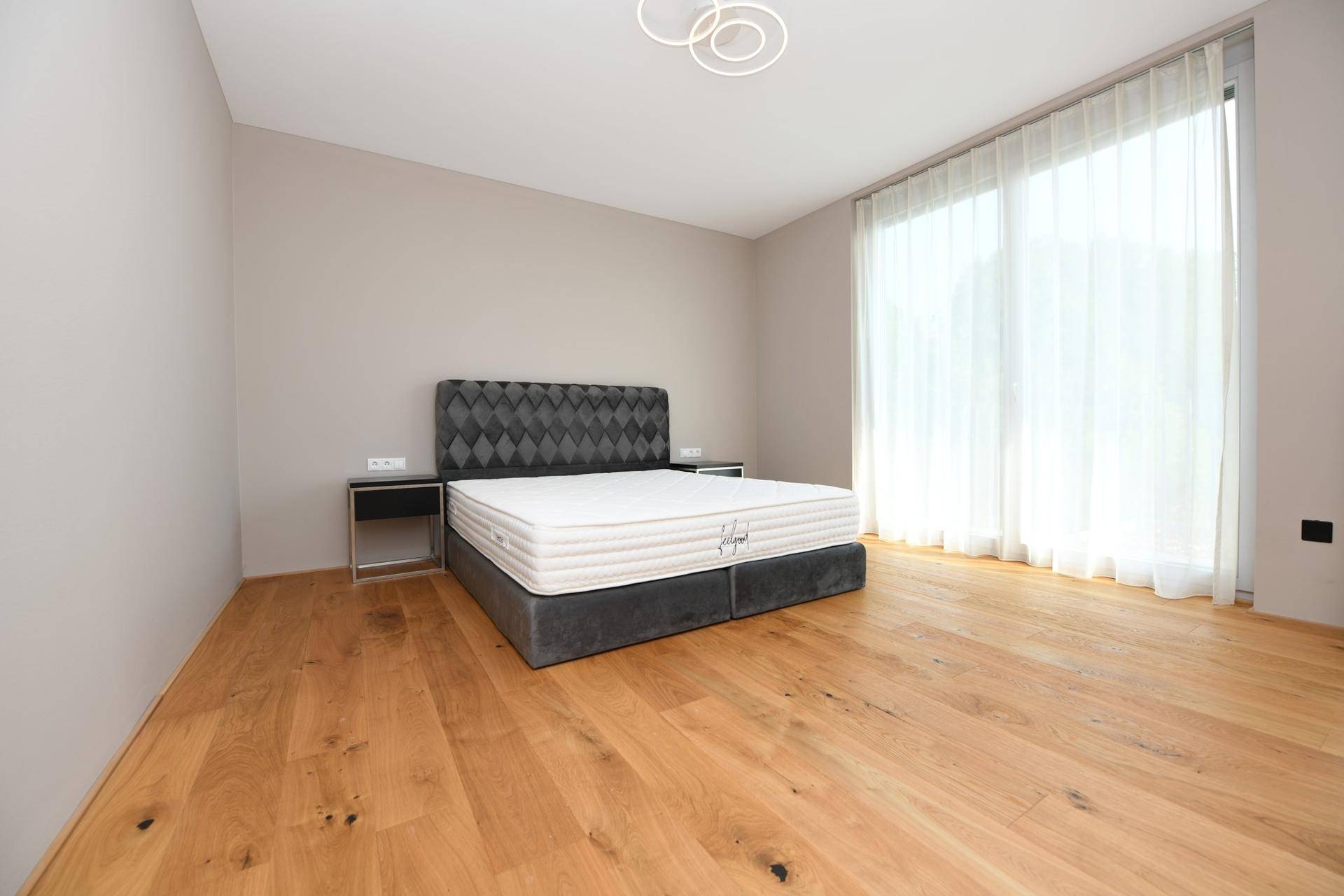 Geräumiges Schlafzimmer mit Holzboden, großem Fenster und modernem Bett.