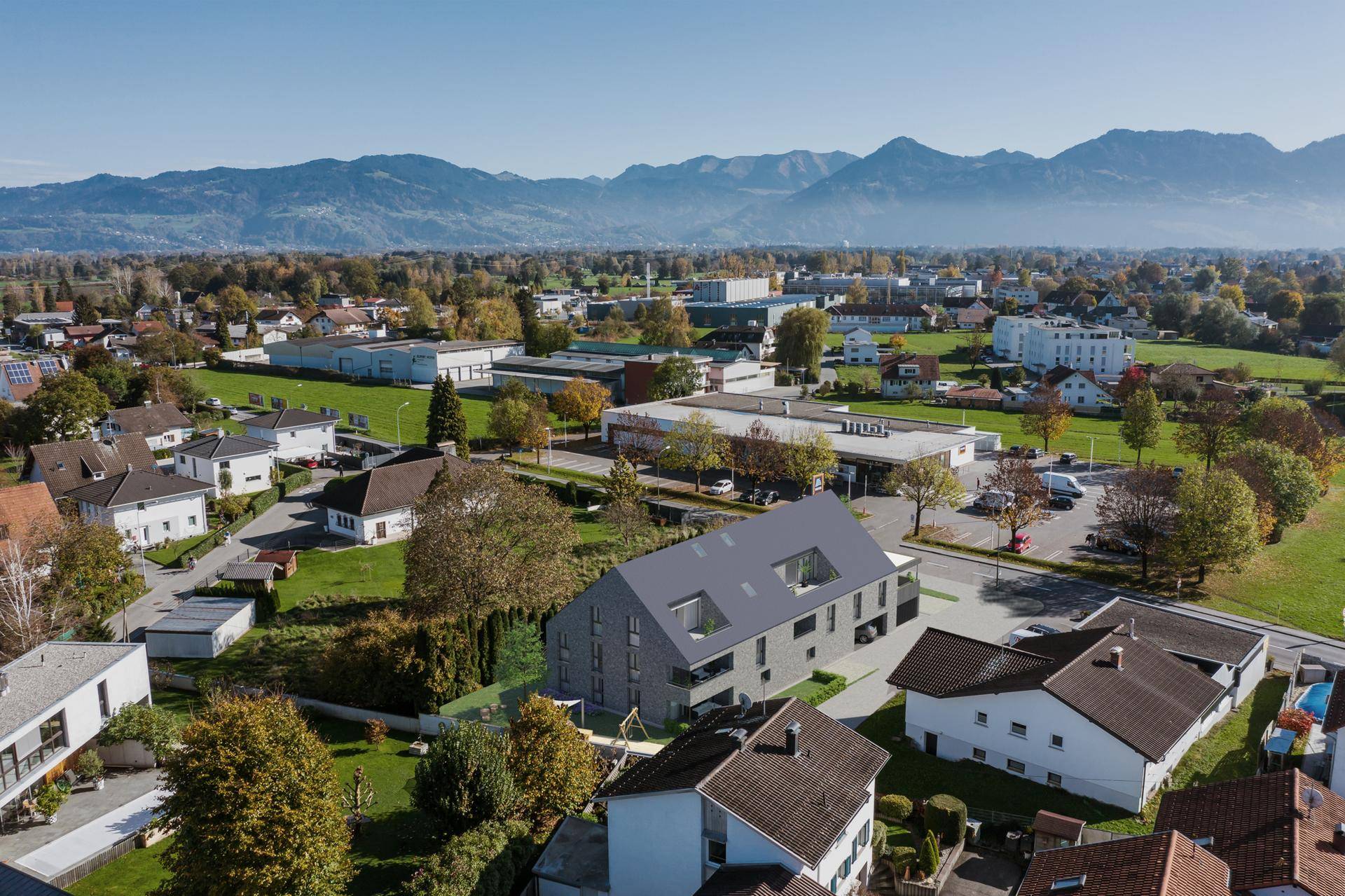 Weitläufige Luftaufnahme des Neubaus eingebettet in eine grüne Landschaft mit Bergsicht.