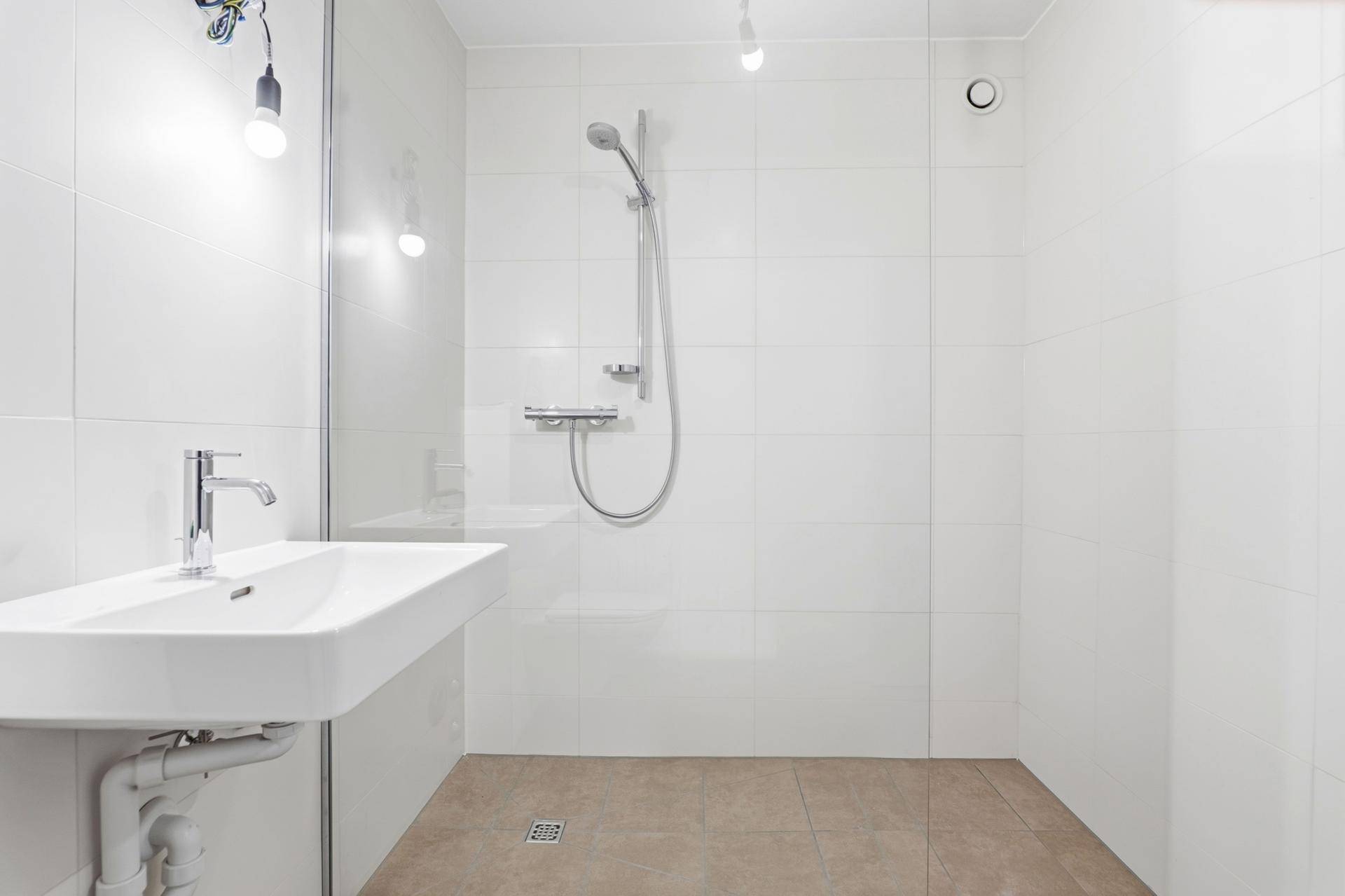 Helle, moderne Dusche mit Glaswand und weißem Waschbecken in einem gefliesten Bad.