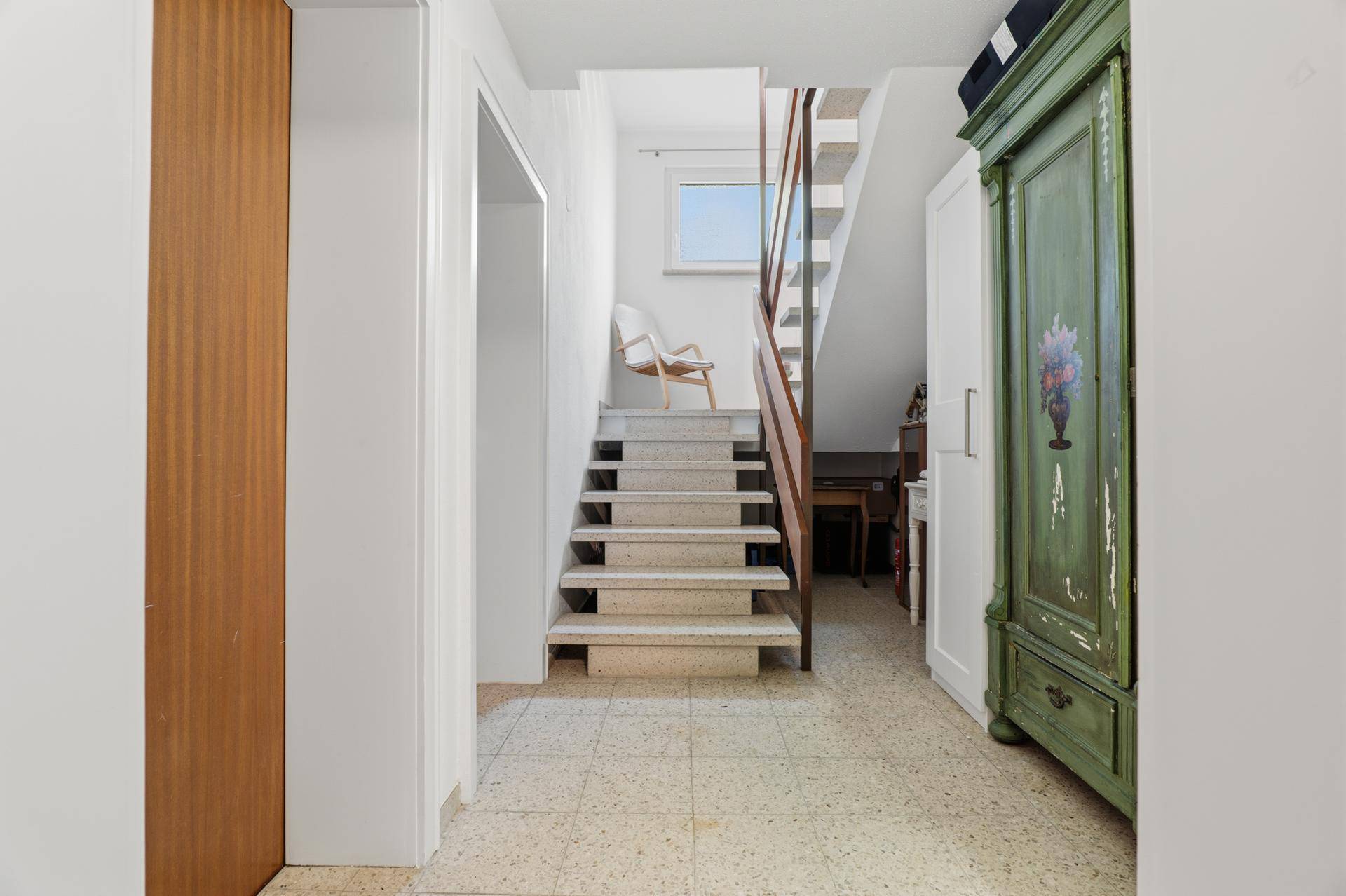 Heller Flur mit Terrazzoboden, Treppe und einem dekorativen grünen Schrank.