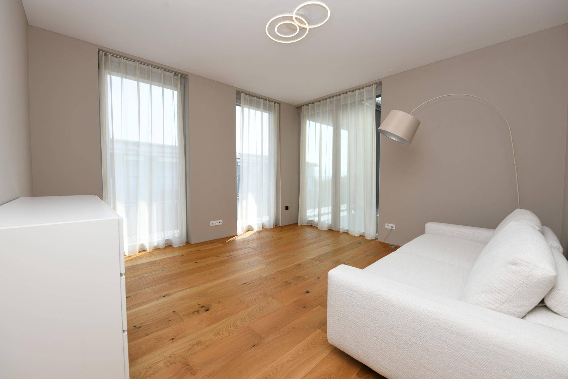 Helles Zimmer mit Holzboden, weißem Sofa und großen Fenstern für viel Tageslicht.