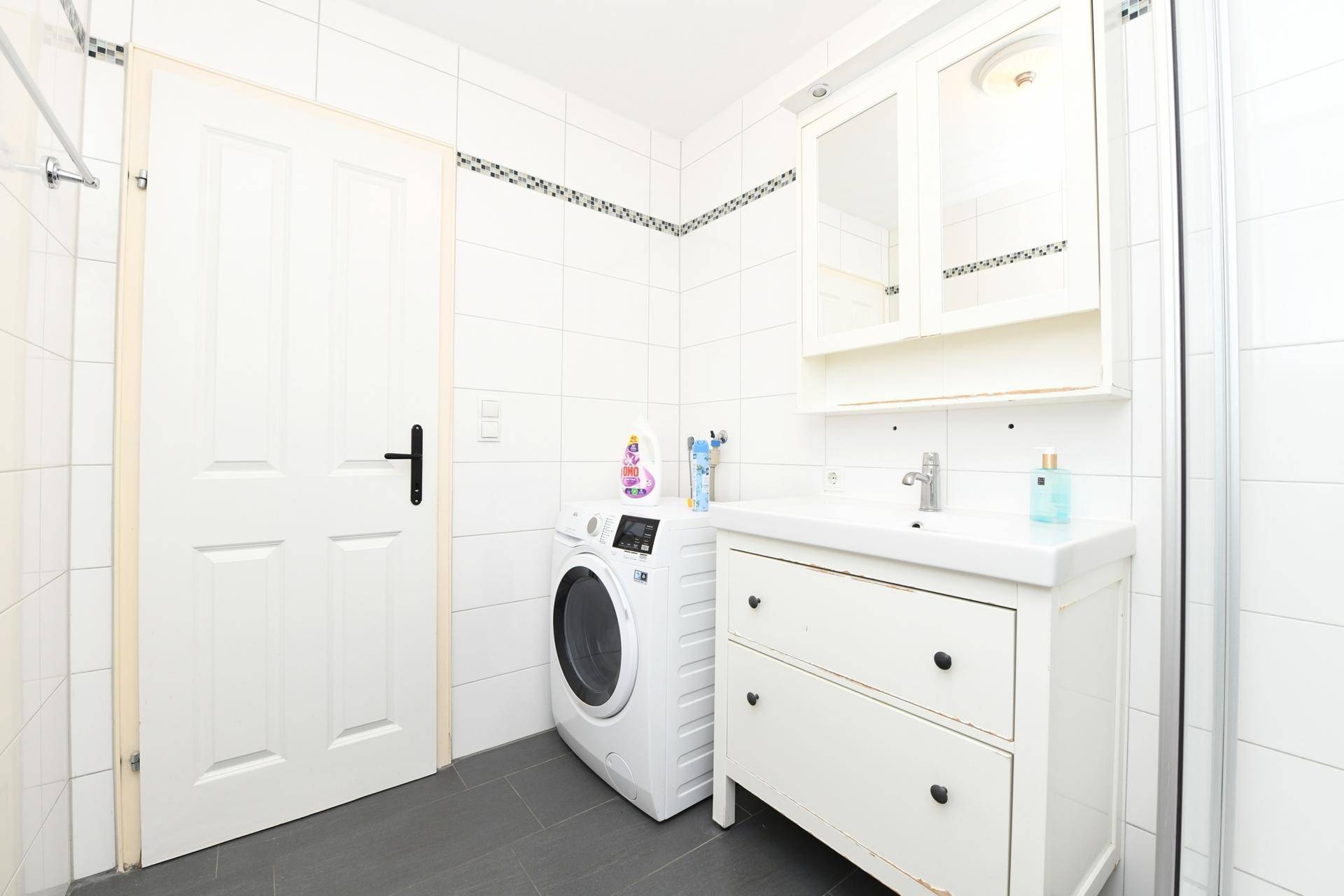 Helles Badezimmer mit Duschkabine, Waschbecken und Waschmaschine.