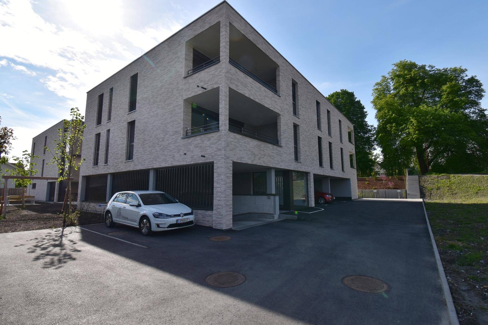 Neubau-Wohngebäude mit moderner Fassade und Außenparkplätzen vor dem Eingangsbereich.