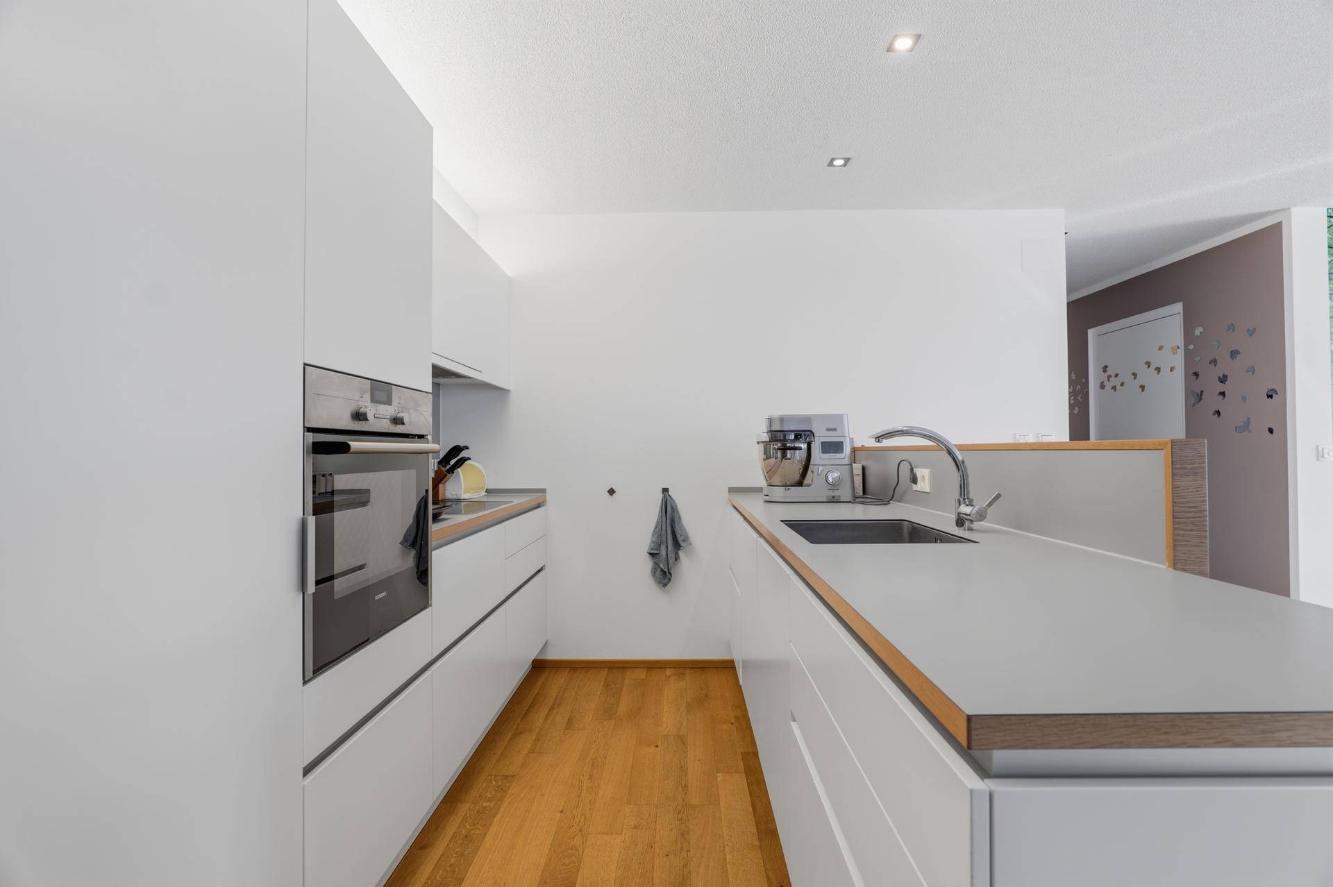 Moderne Küche mit weißen Fronten, grauer Arbeitsplatte und integrierten Geräten.