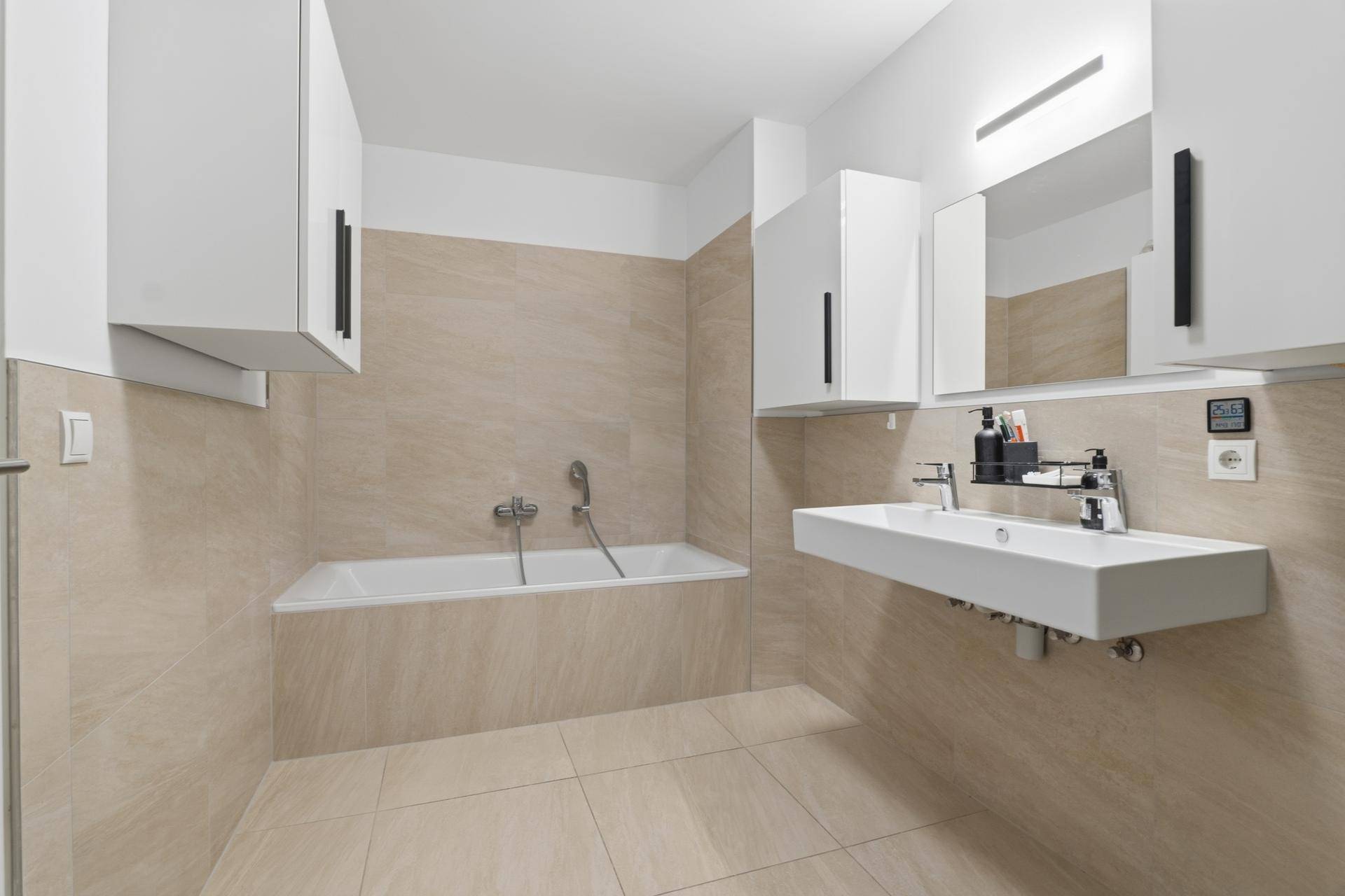 Helles Badezimmer mit Badewanne, modernem Waschbecken und eleganten beigefarbenen Fliesen.