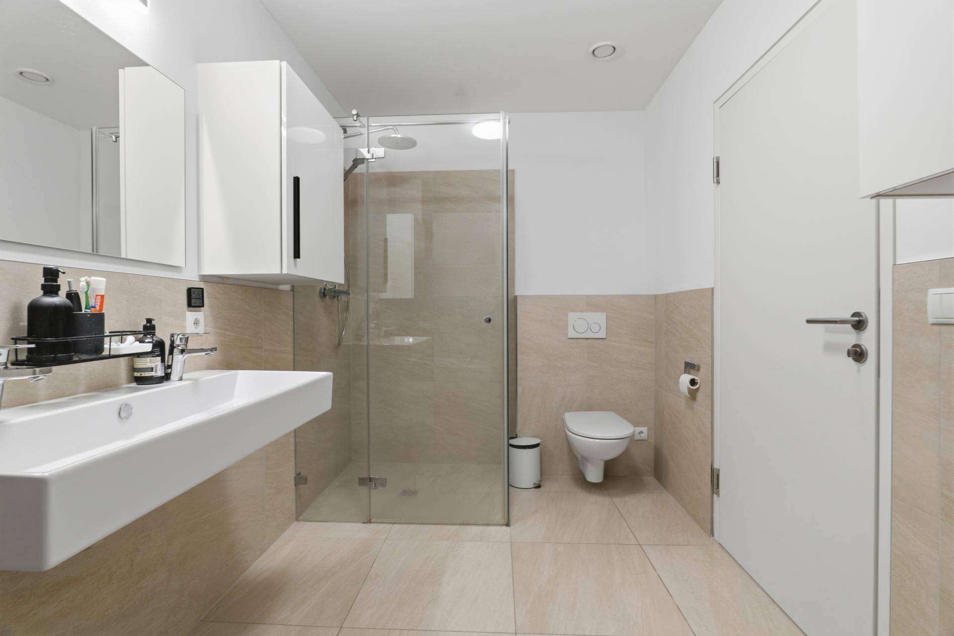 Zeitgemäßes Badezimmer mit begehbarer Dusche, Regenbrause, Wand-WC und modernem Waschbecken.