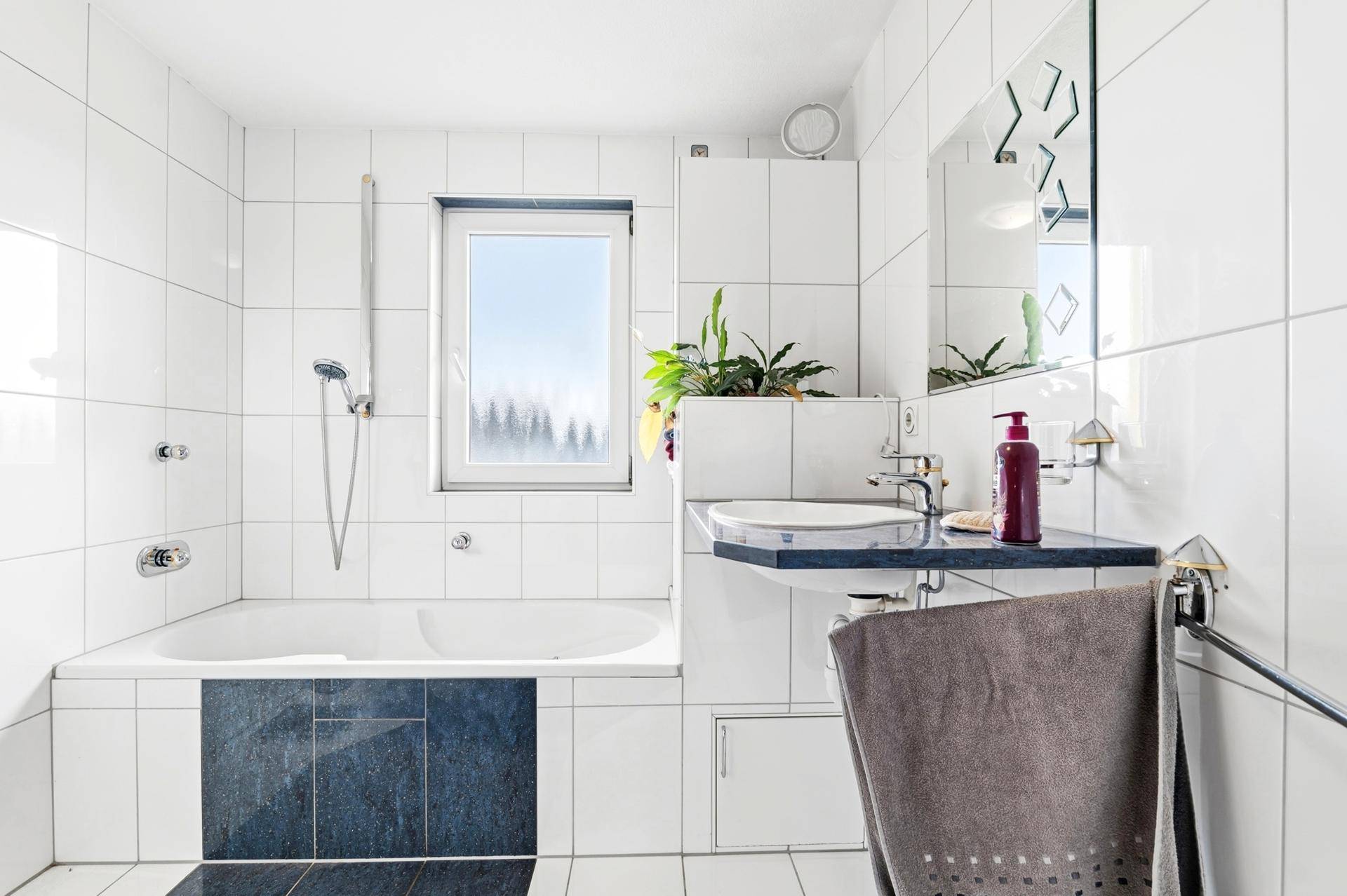 Helles Badezimmer mit Badewanne, Dusche, Waschbecken und Fenster.