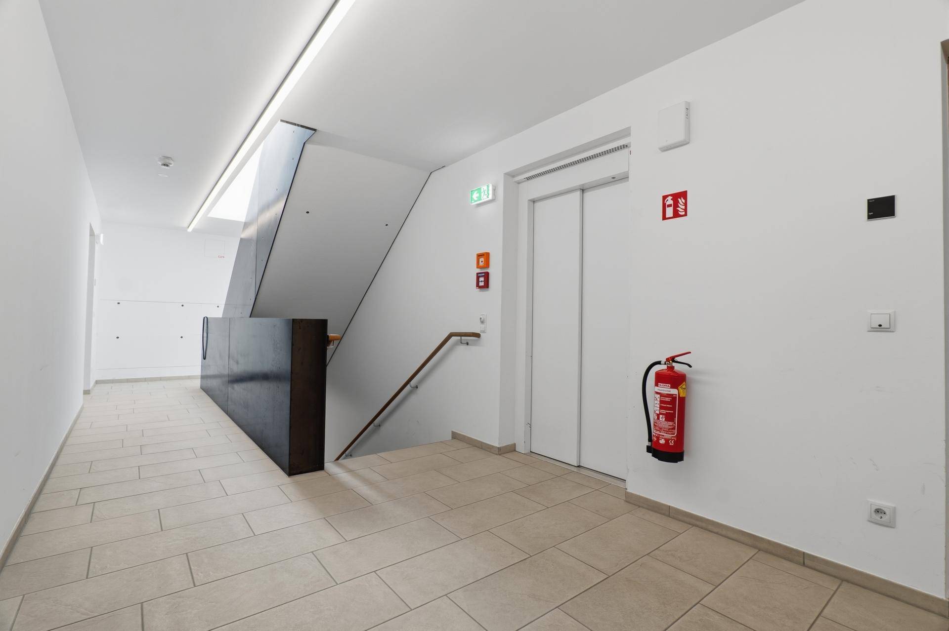 Gemeinschaftsbereich im Gebäude mit Treppenhaus, Aufzug und gefliestem Boden.