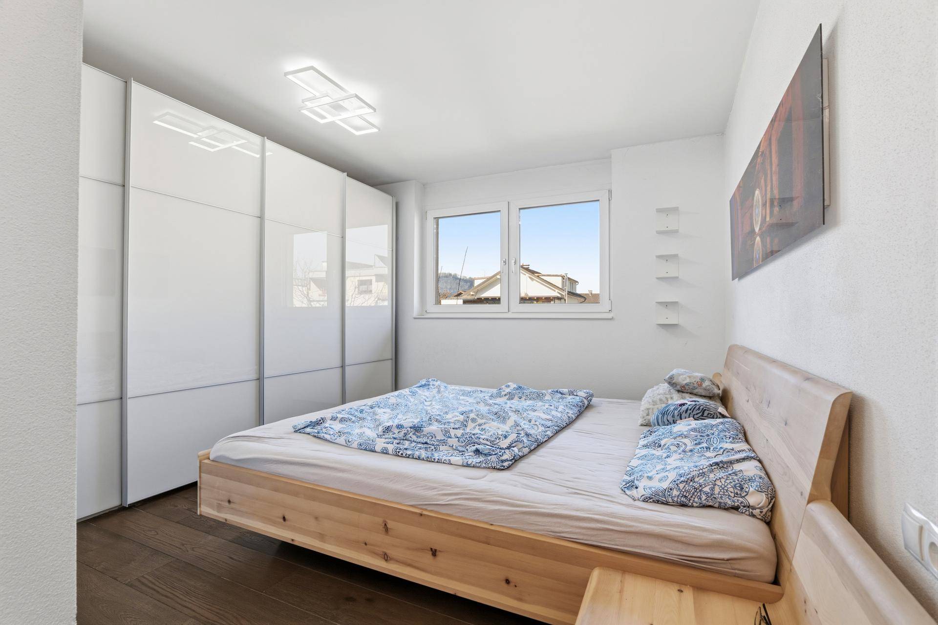 Schlafzimmer mit Holzbett, weißen Schränken und Fensterblick.