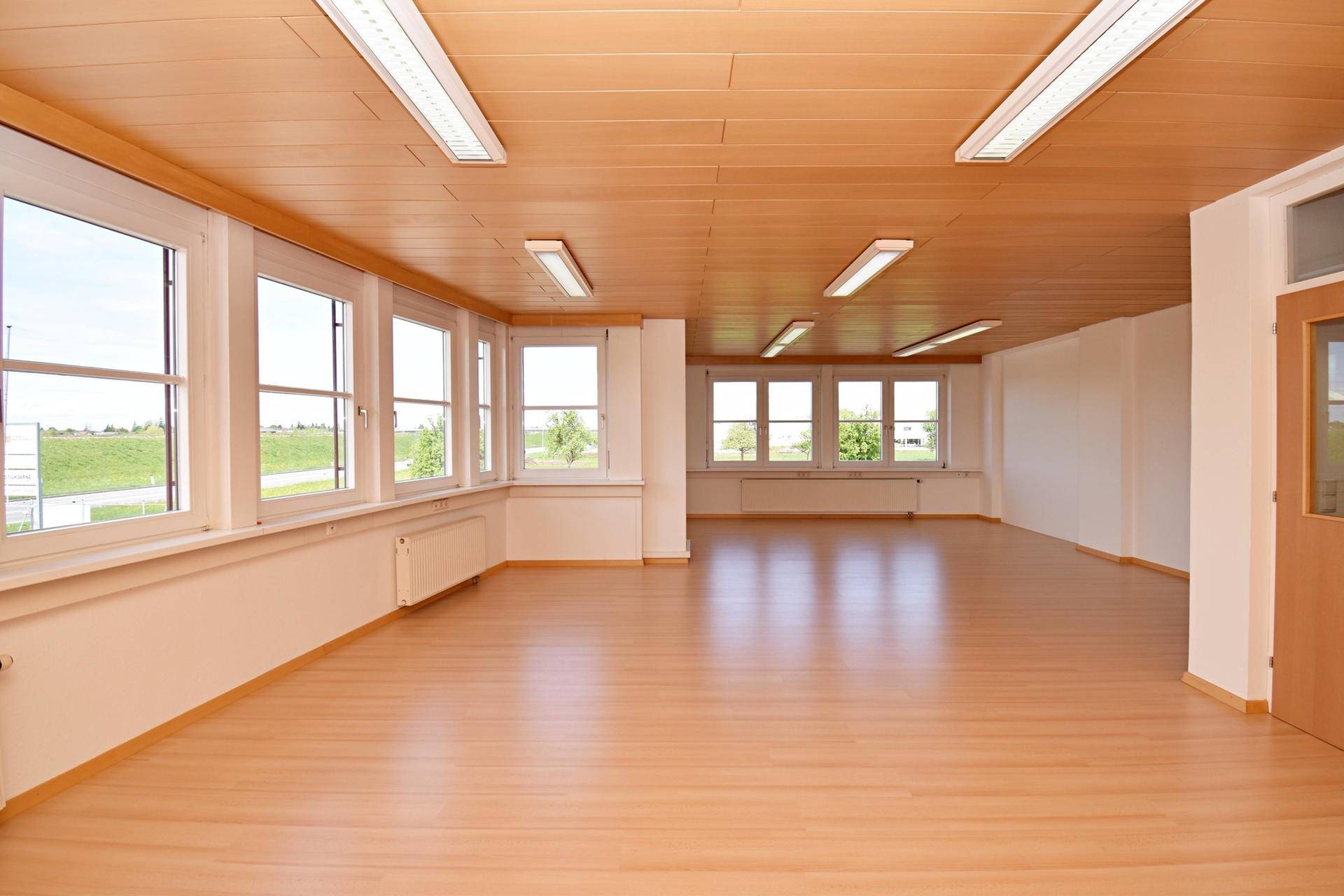 Geräumiges, helles Büro mit Laminatboden, Holzdecke und Fenstern mit Weitblick.