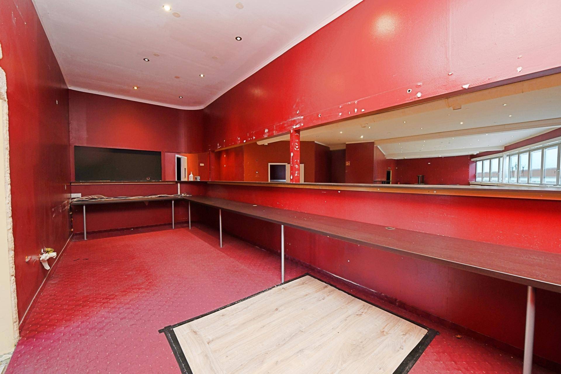Lounge-Bereich mit rotem Teppichboden, Spiegelwand und langen Ablageflächen, ideal für Veranstaltungen.